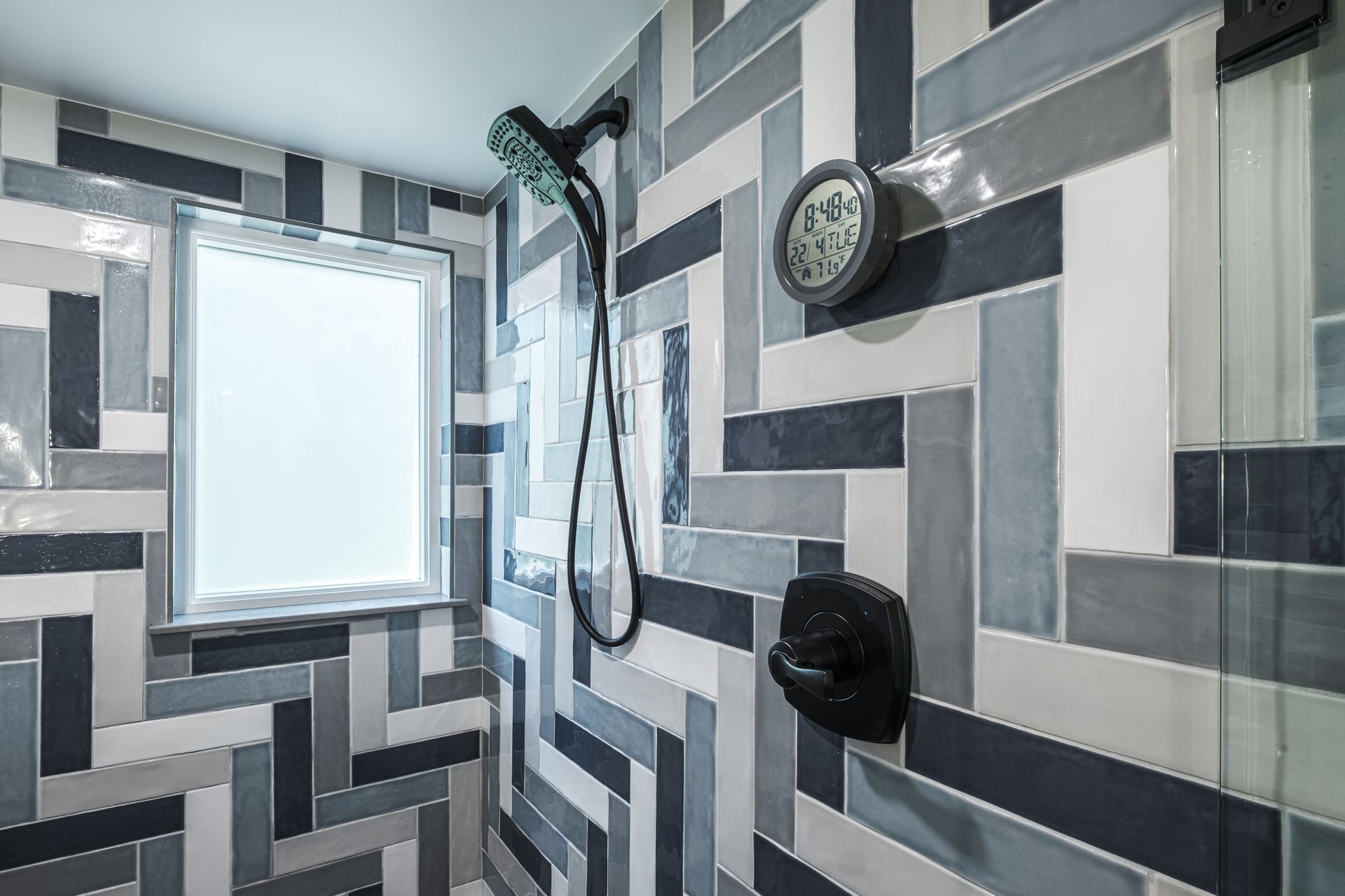 Shower with blue, gray, and white herringbone tile, black fixtures, and a small window.