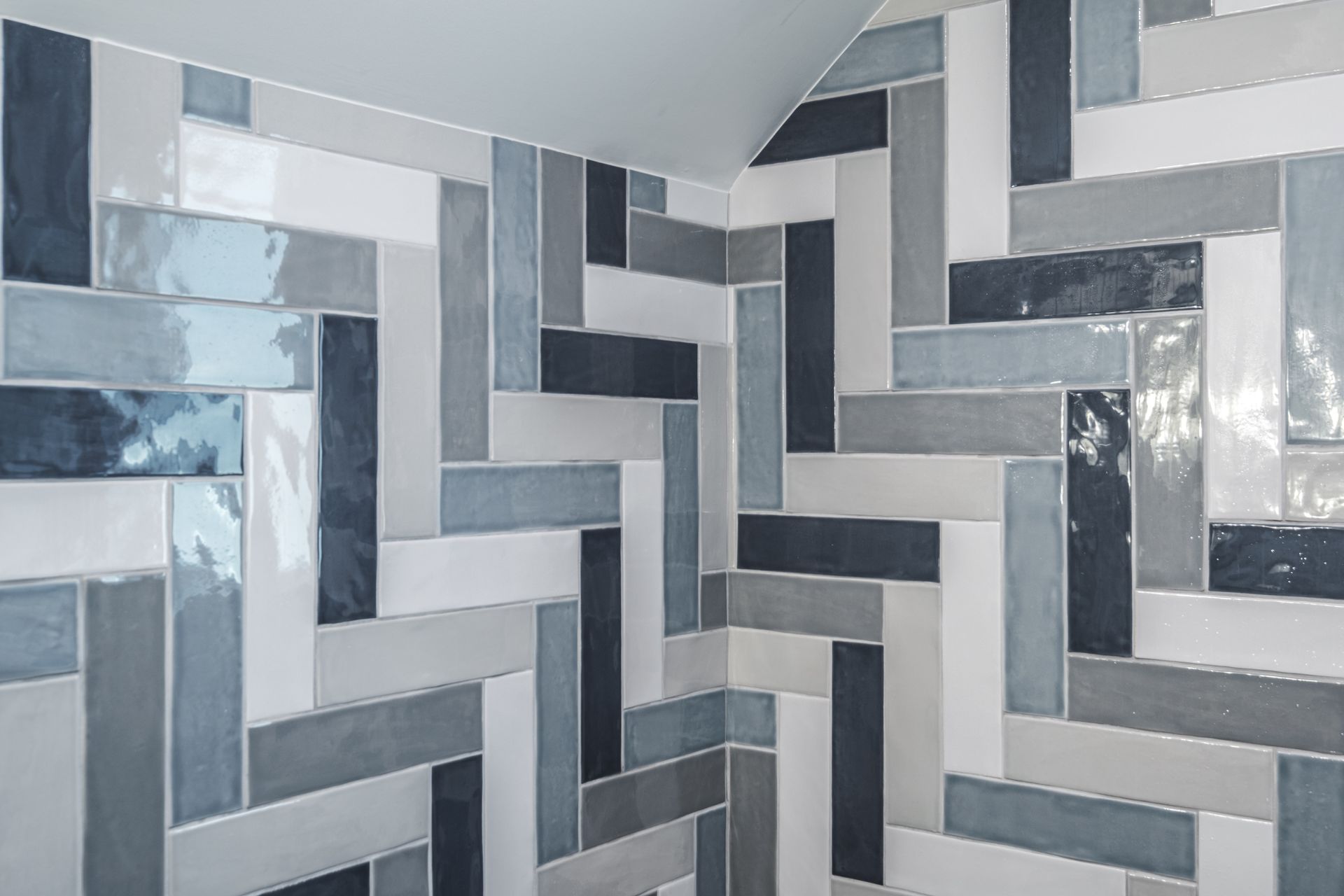 Herringbone pattern tiles in various shades of blue, gray, and white on a corner wall.