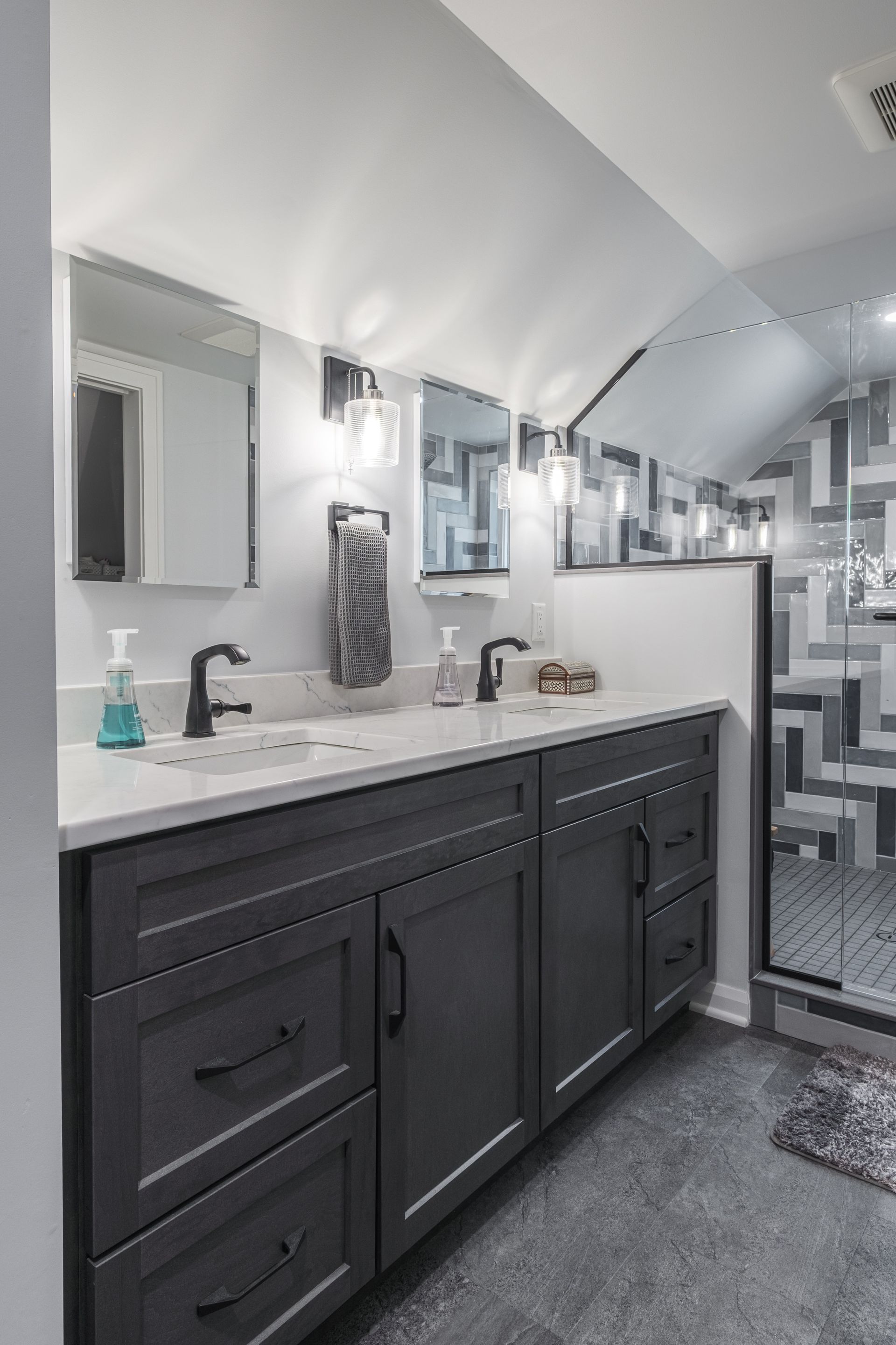 Gray bathroom with double vanity, black fixtures, and geometric shower wall.