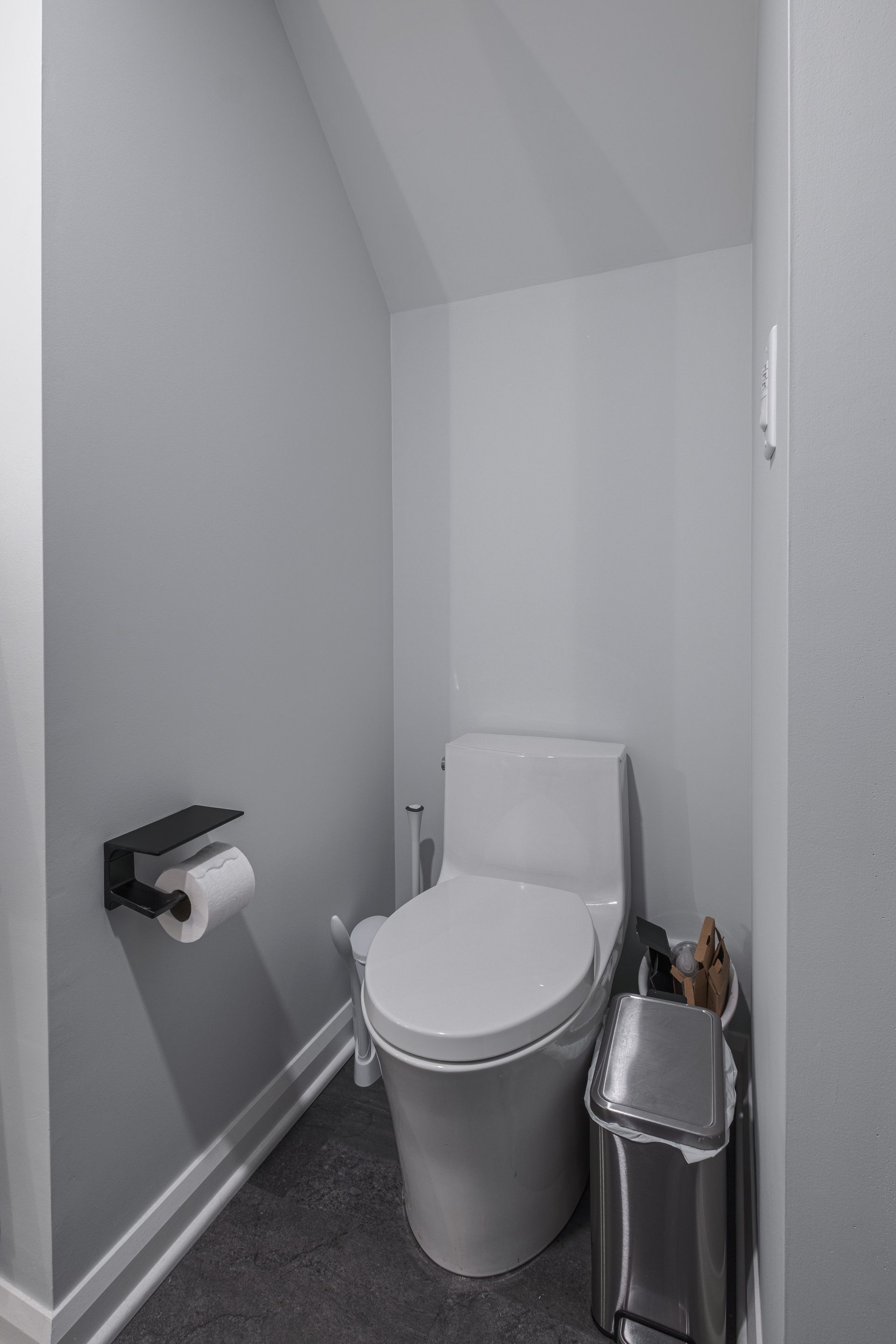 Small, gray bathroom with a modern toilet and a black toilet paper holder.