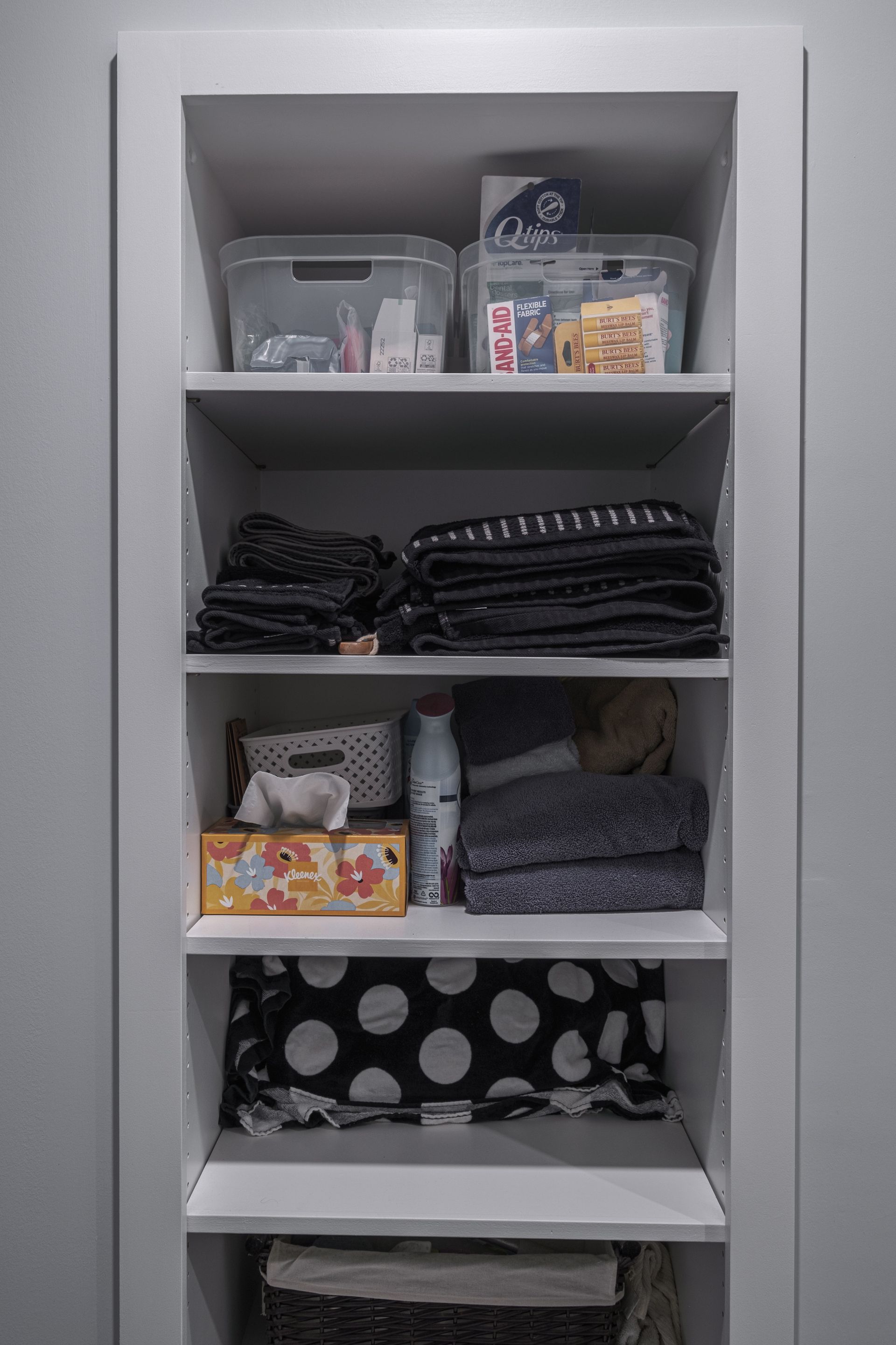Built-in shelves with neatly organized items: containers, clothes, tissues, and a basket. White shelves, gray background.