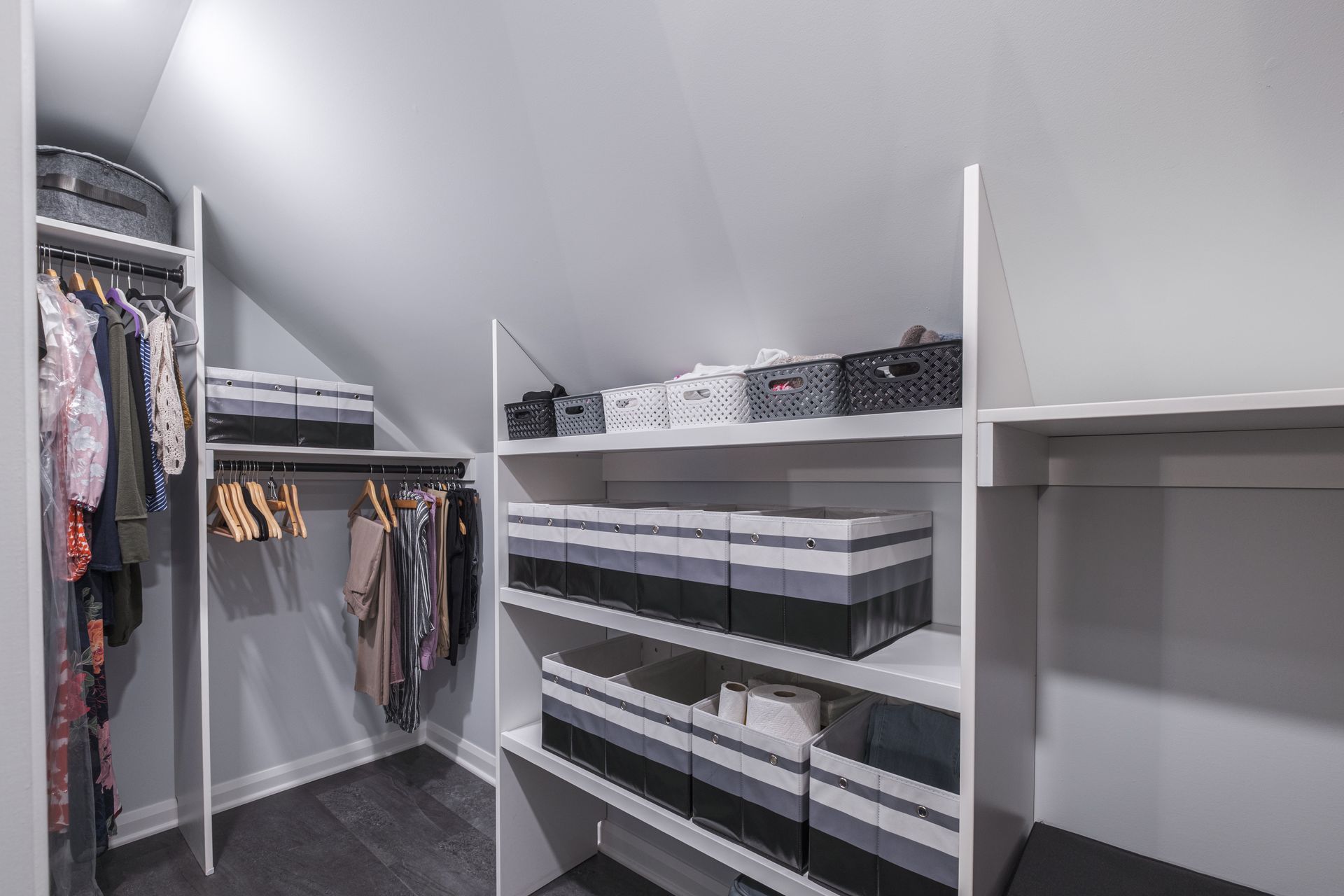 A walk-in closet with shelves and hanging rods; gray and white color scheme; storage boxes neatly arranged.