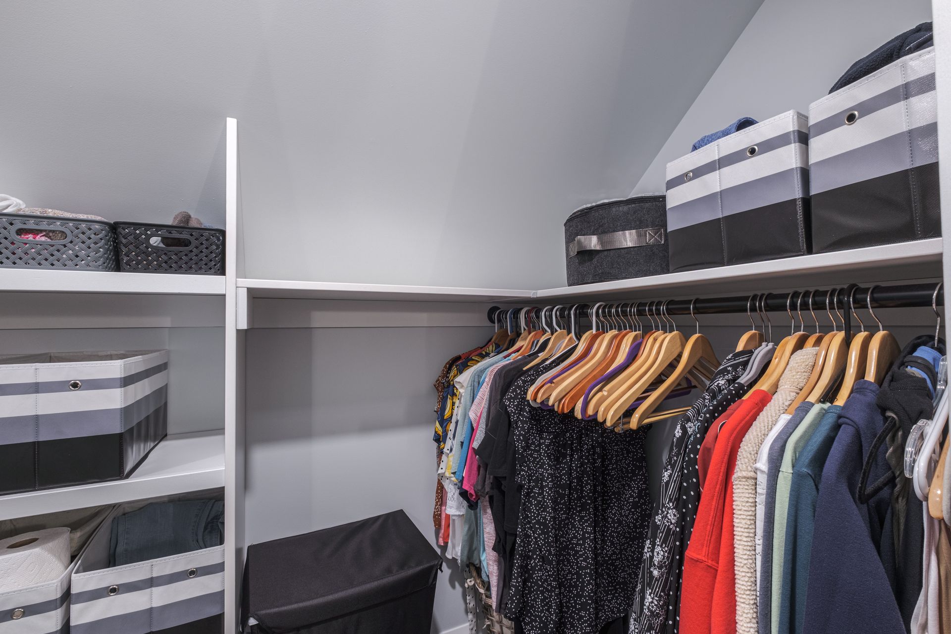 Closet interior with clothes on hangers, shelves with storage boxes, and slanted ceiling.