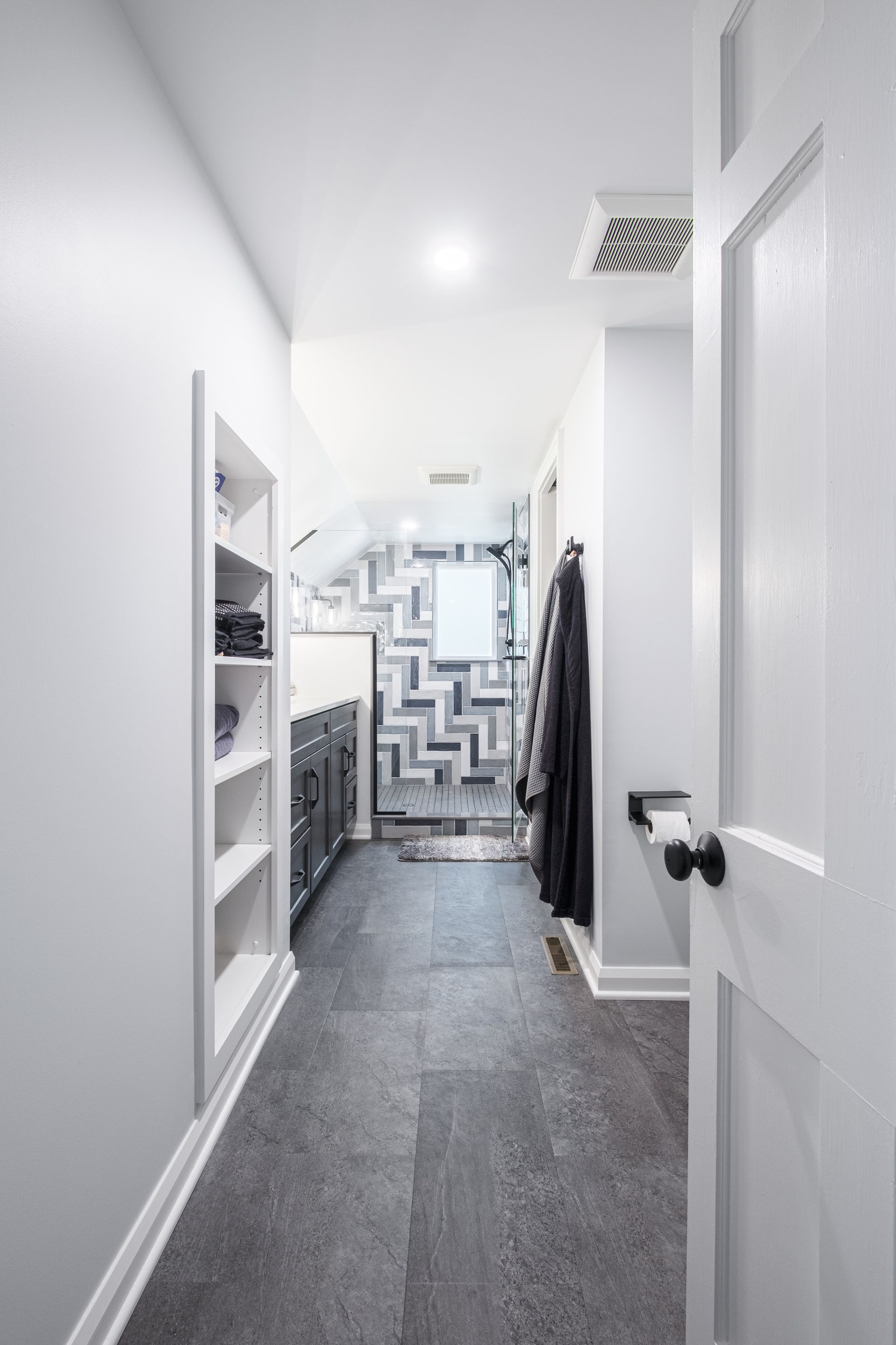 Narrow hallway with gray flooring, built-in shelves, and coat rack. White door on the right.