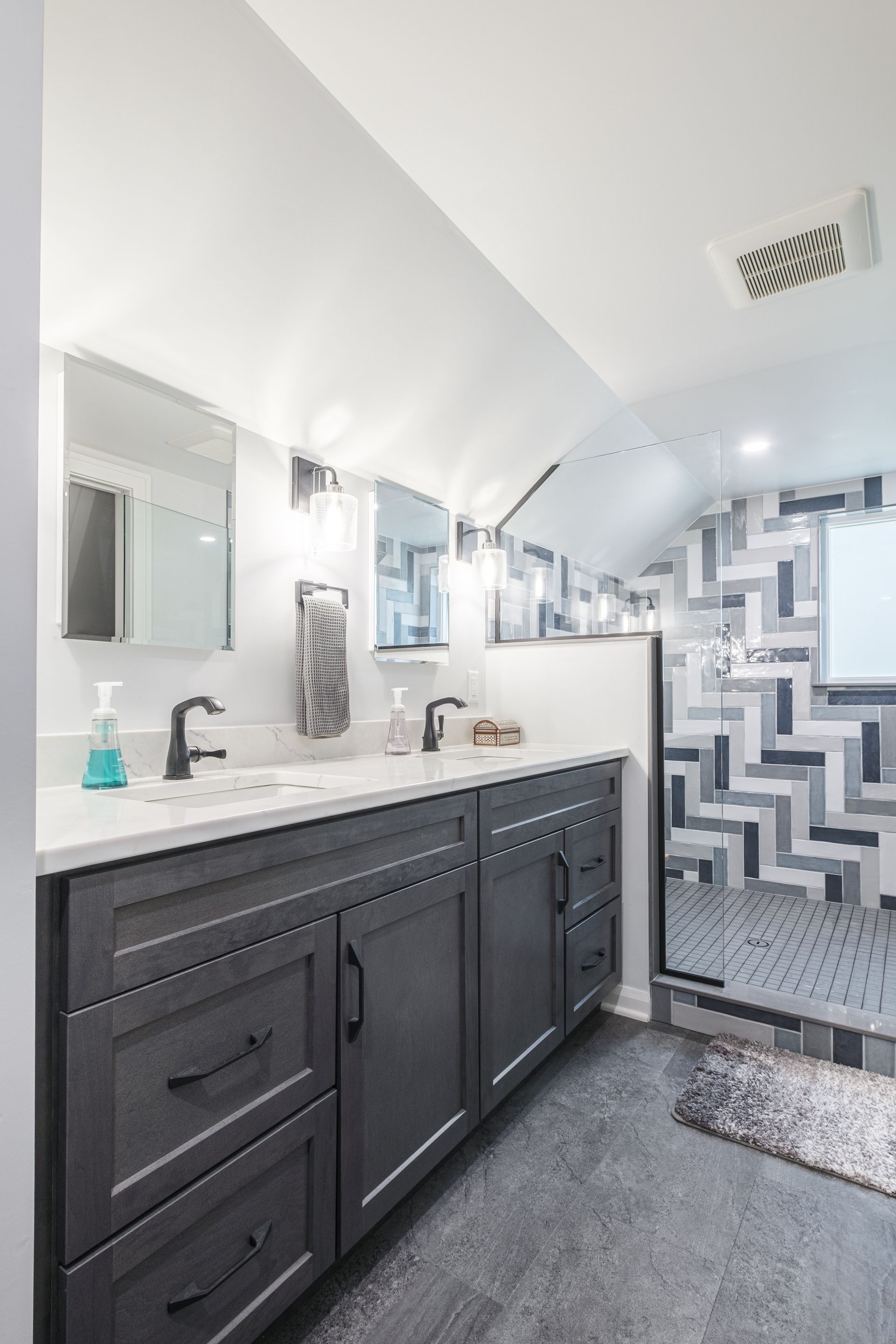 Modern bathroom with gray vanity, white countertop, and patterned shower tile.