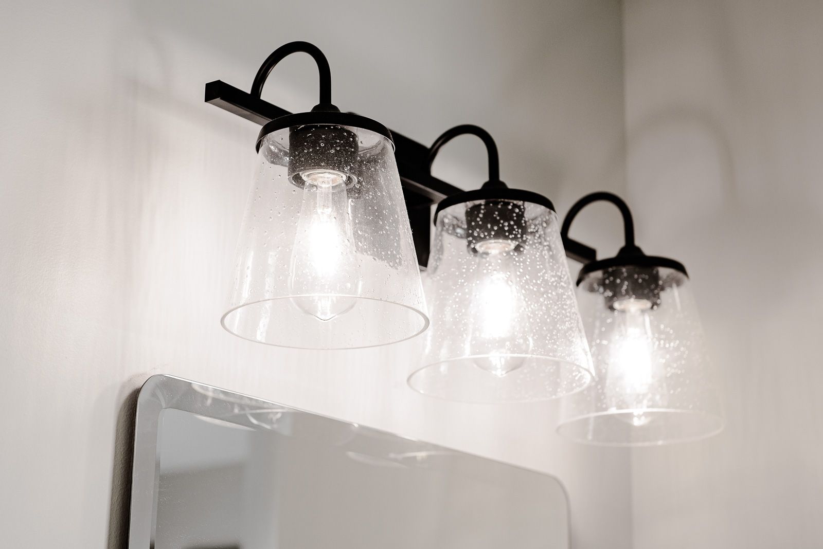 A bathroom vanity light with clear glass shades hanging over a mirror.