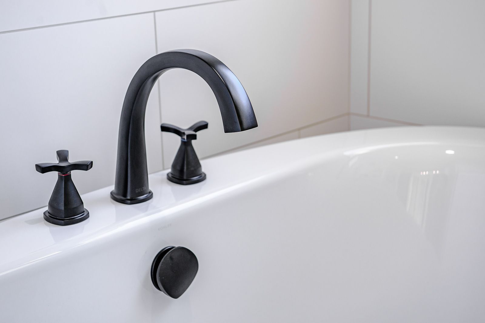 A black faucet is sitting on top of a white bathtub.