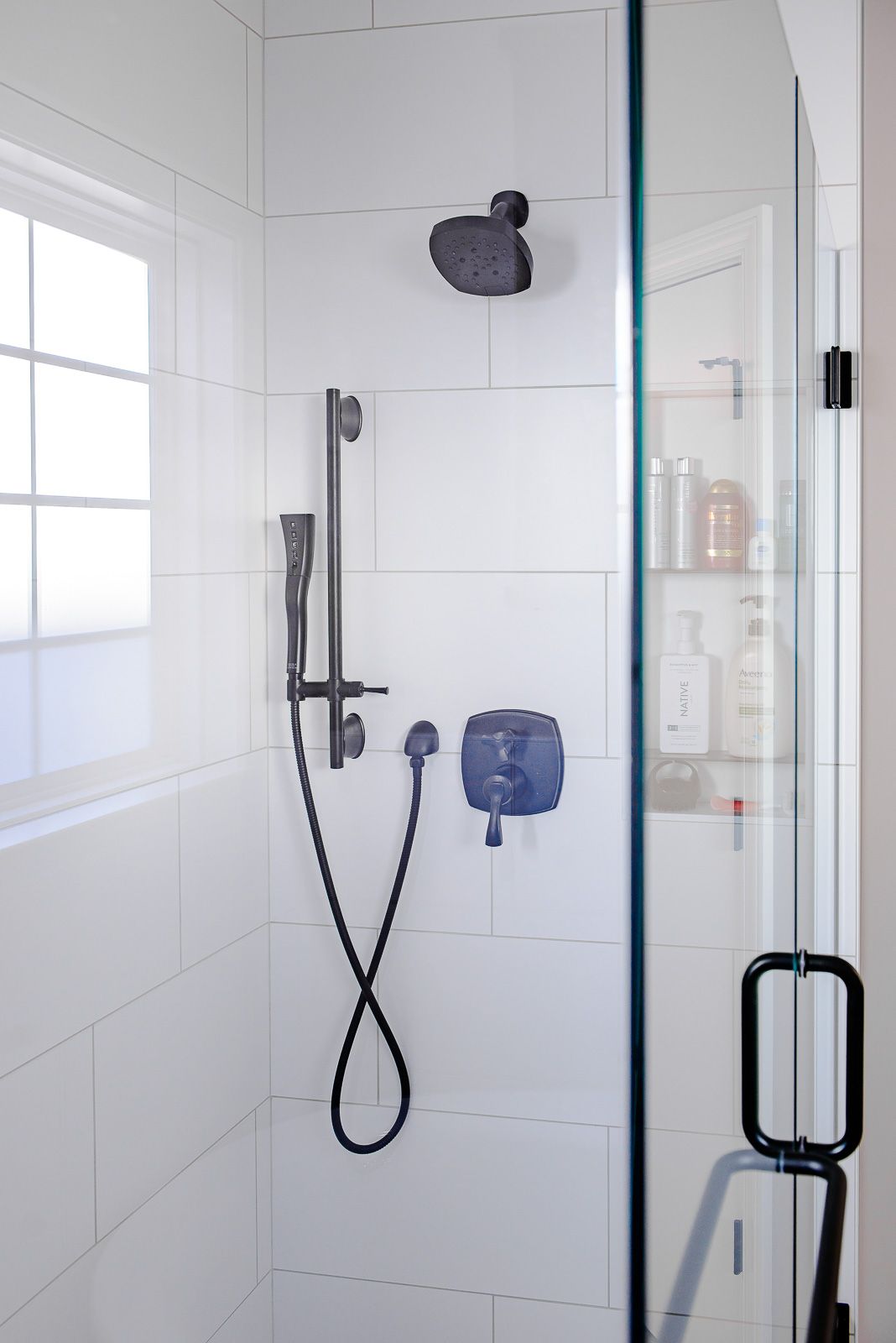 A shower with white tiles and a black shower head