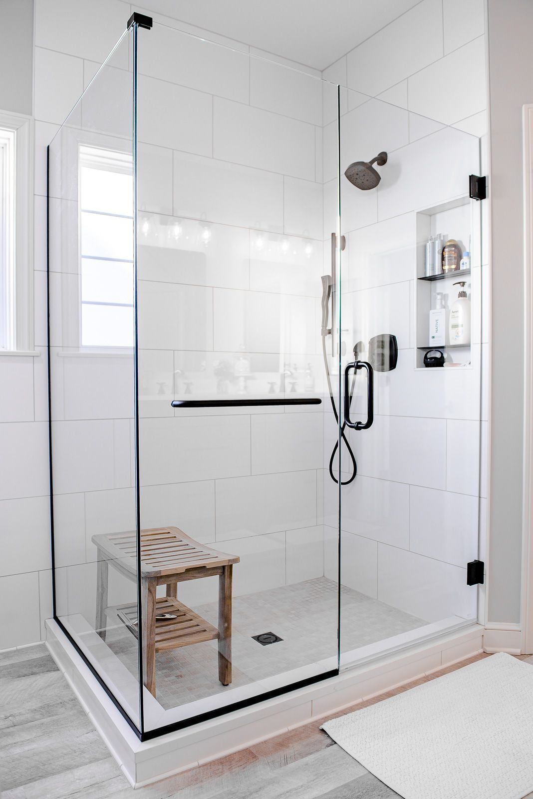 A bathroom with a walk in shower with a glass door and a wooden bench.