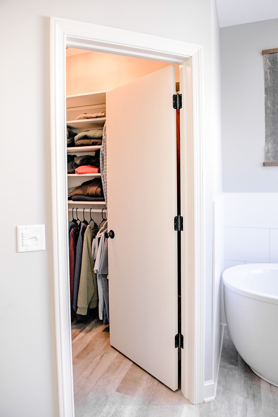A walk in closet in a bathroom next to a bathtub.