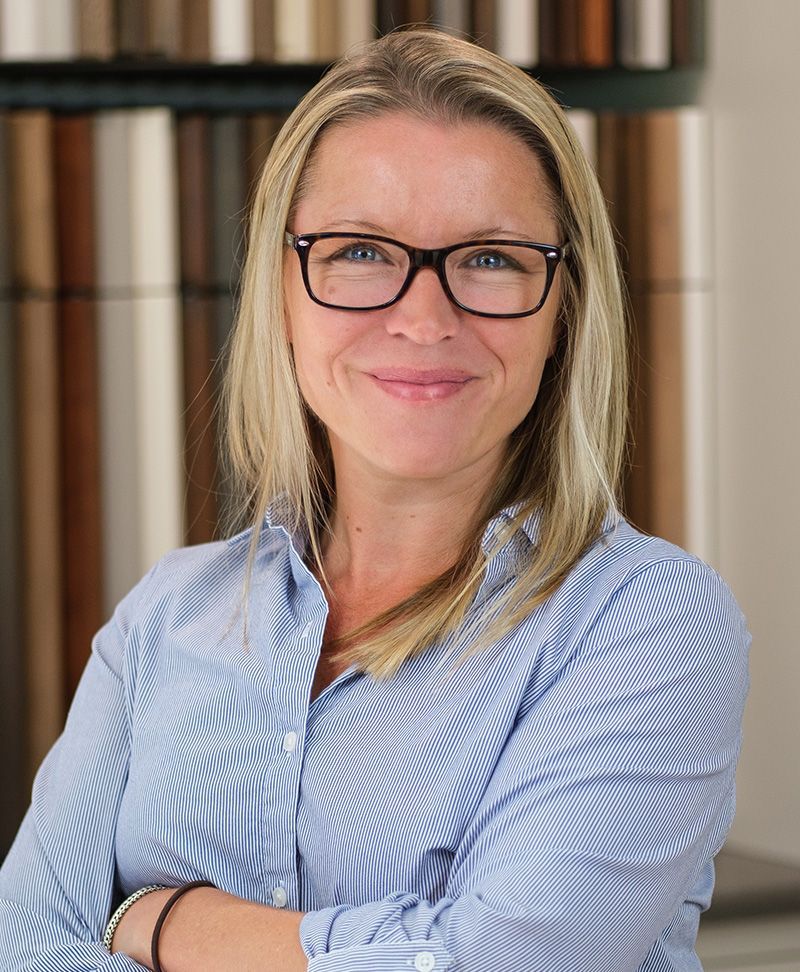 Blonde woman in blue striped shirt and glasses smiles with arms crossed.