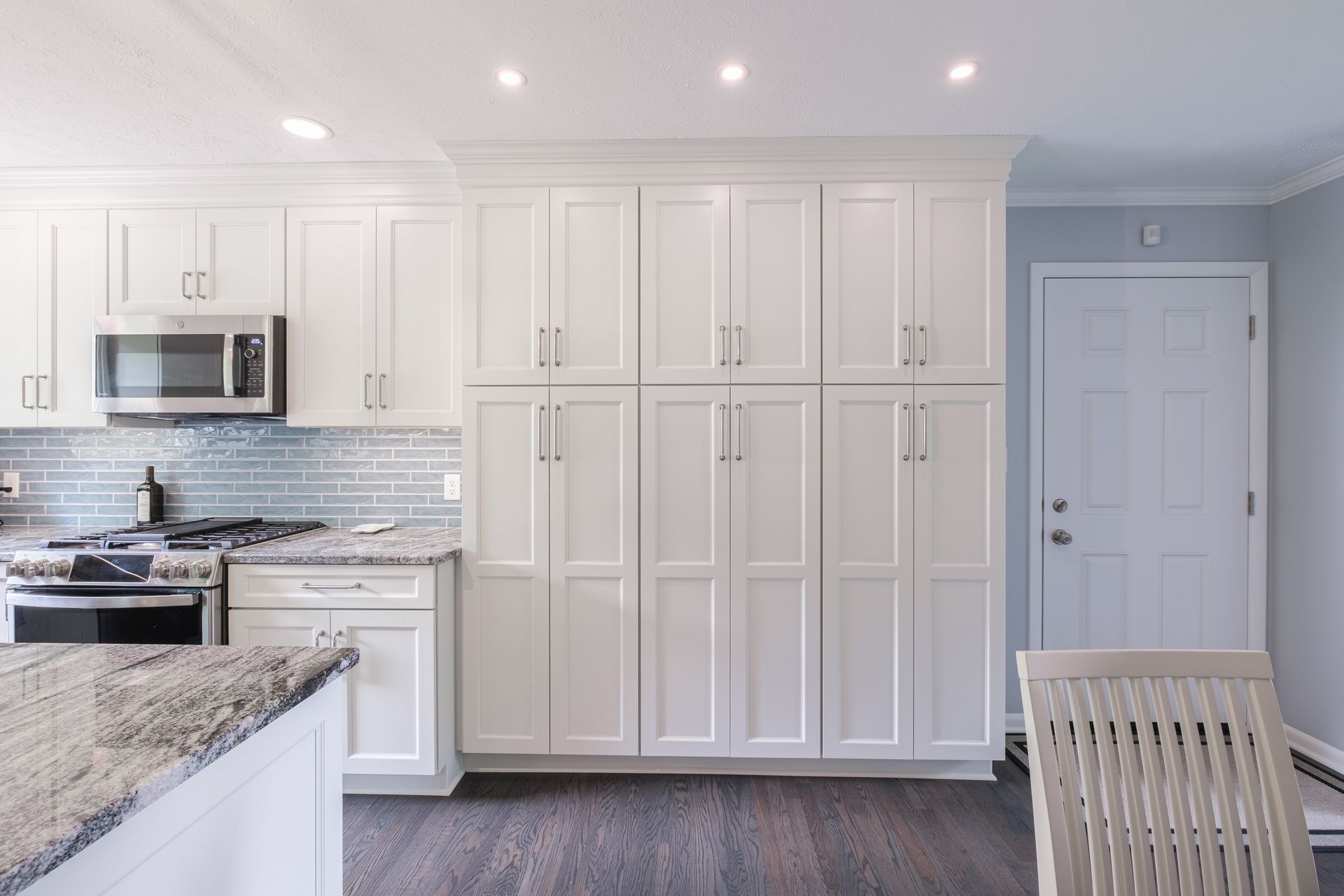 White kitchen with large cabinets, microwave, stove, island, and door.