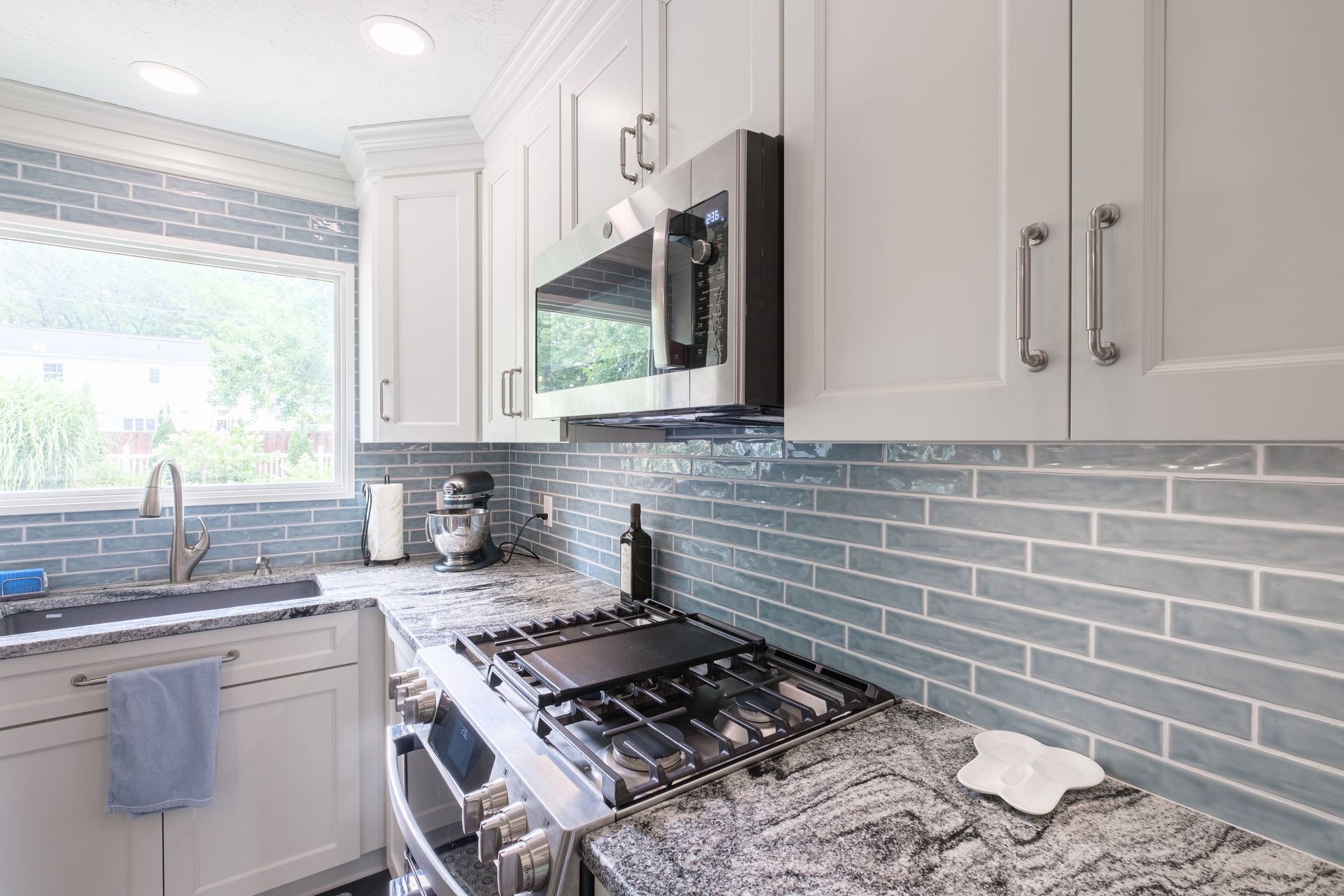 White kitchen with blue tile backsplash, stainless steel appliances, granite countertops.