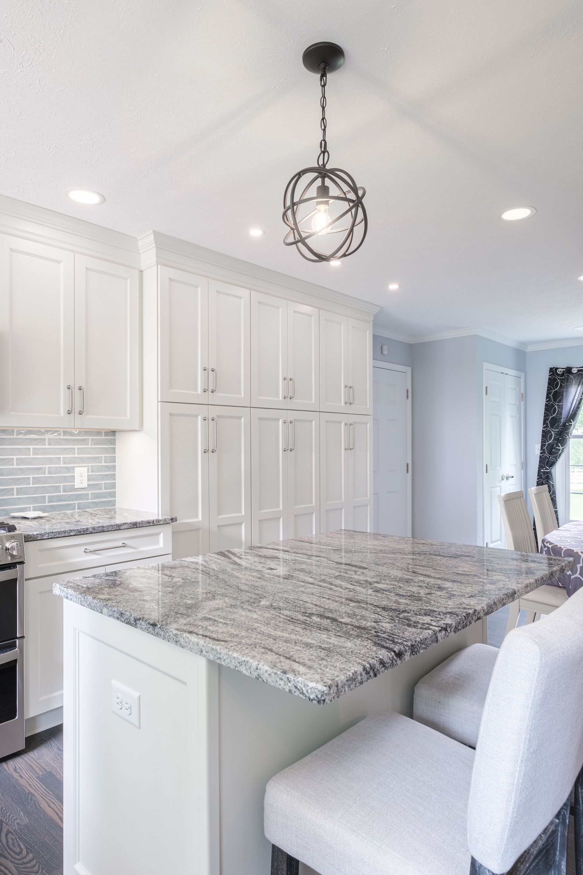 Modern white kitchen with a marble island, pendant light, and matching bar stools.
