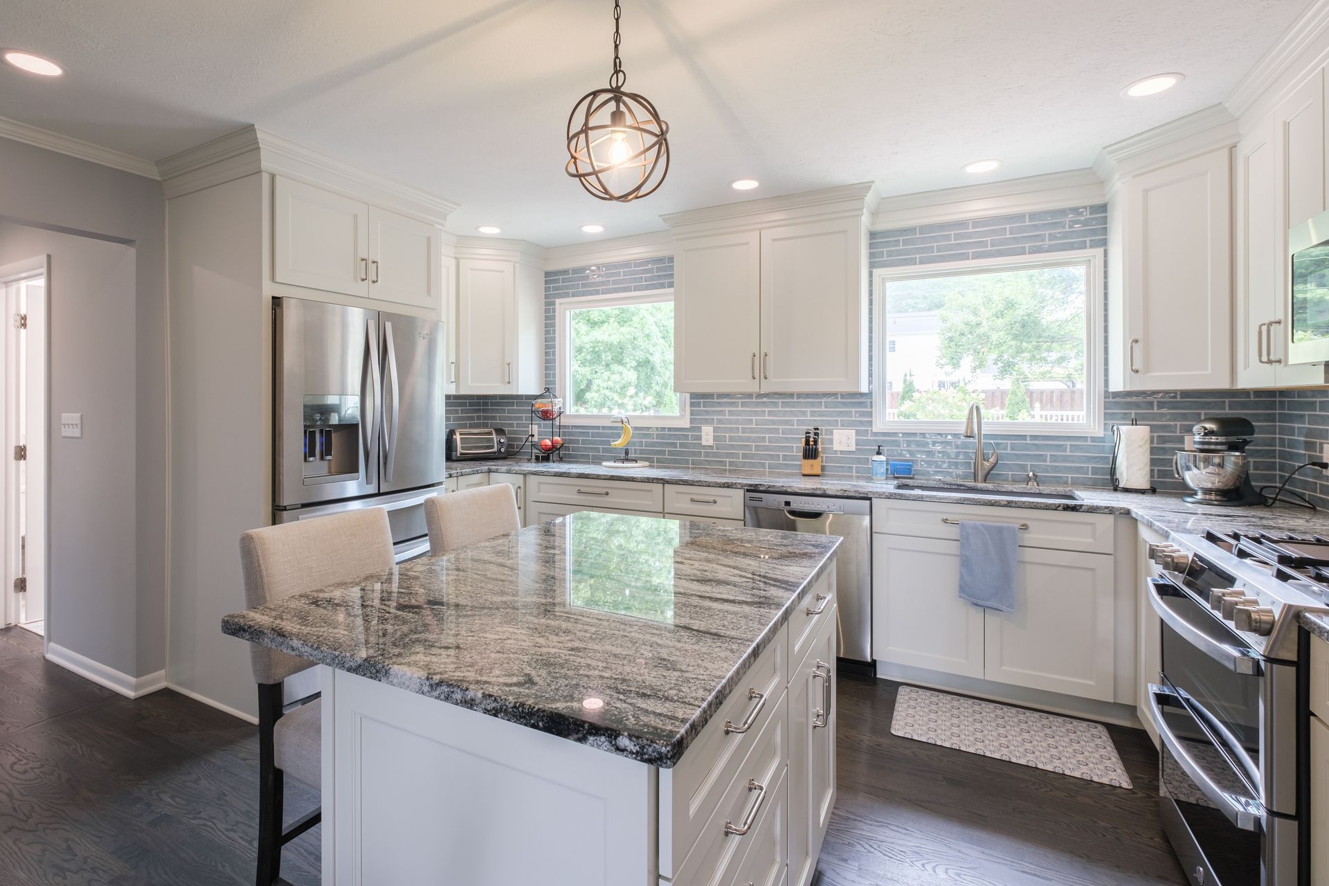 Bright white kitchen with a granite island, stainless steel appliances, and blue backsplash.