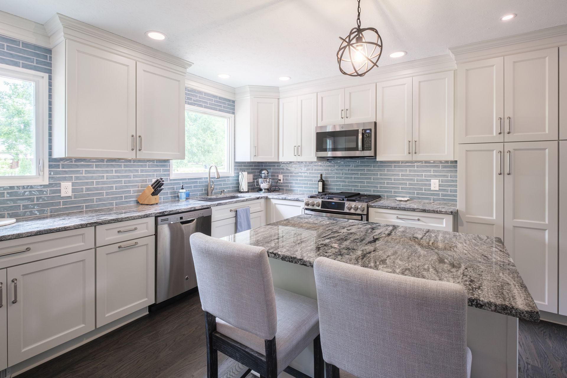 Bright white kitchen with a gray island and backsplash, stainless steel appliances.