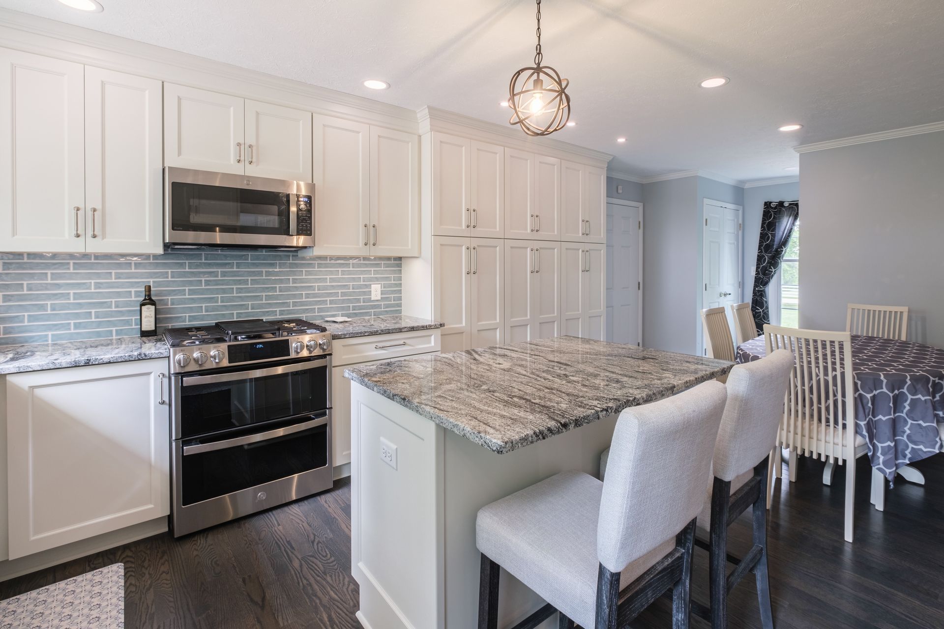White kitchen with stainless steel appliances, granite island, and dining area.