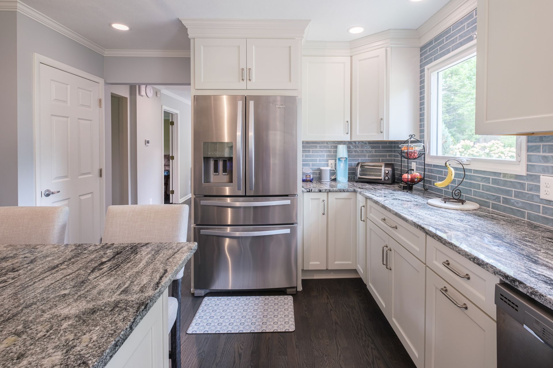White kitchen with stainless steel appliances, grey countertops, and dark wood floors.