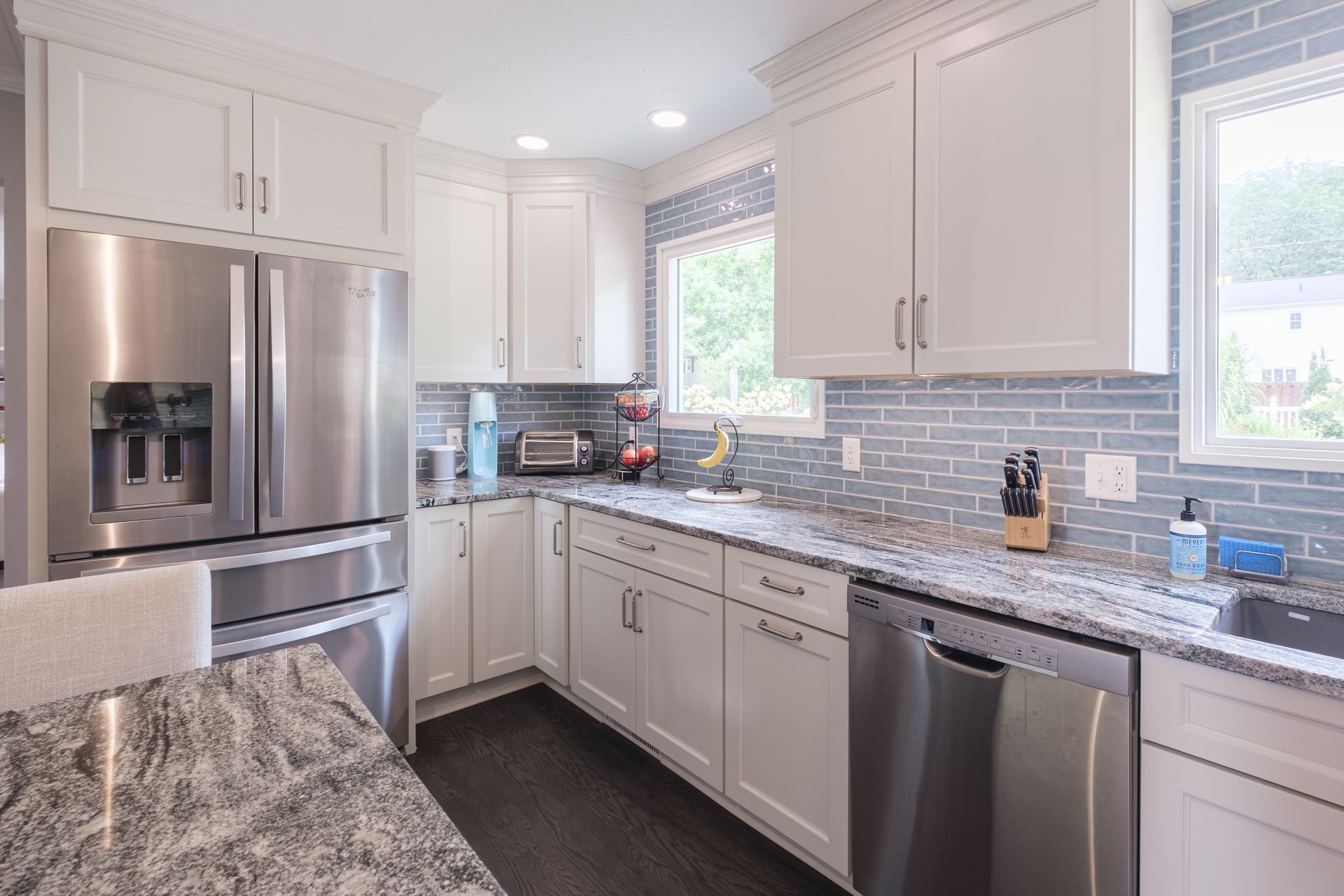 White kitchen with stainless steel appliances, grey backsplash, and granite countertops.