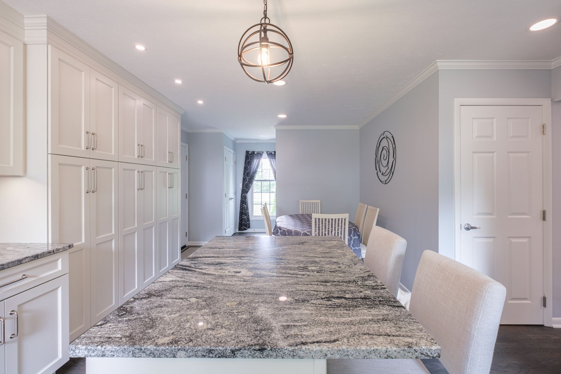 Spacious kitchen with white cabinets, granite island, light blue walls, and a dining table.