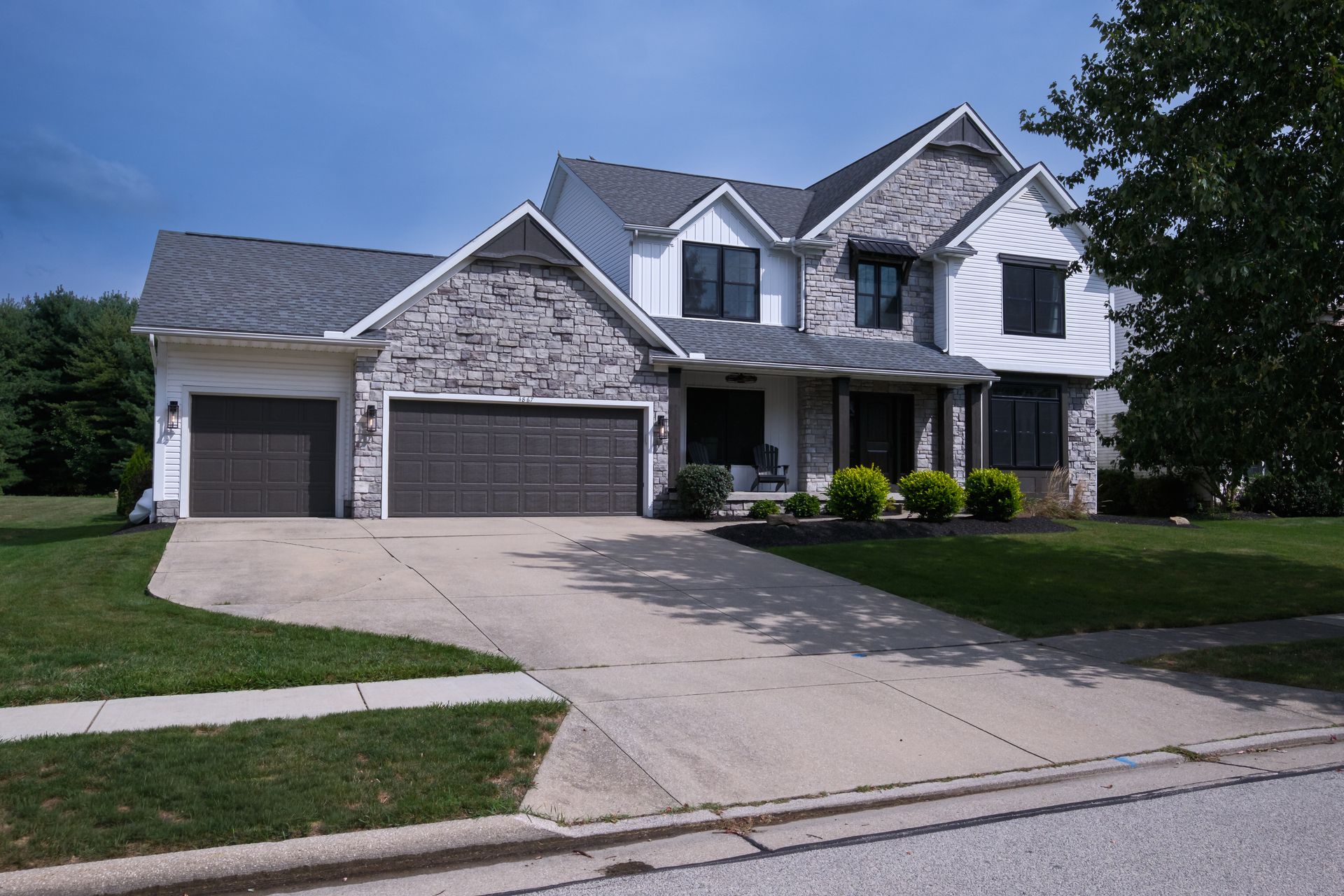 Two-story house with gray brick facade, white siding, and two-car garage. Driveway and green lawn in front.