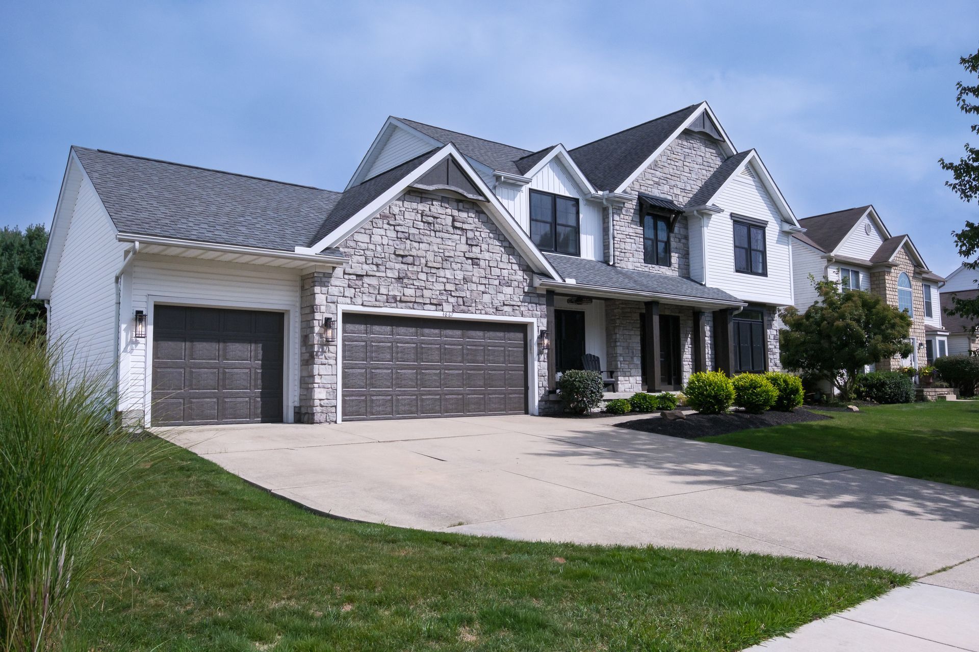 Two-story house with stone and white siding, gray roof, two-car garage, driveway, and green lawn.