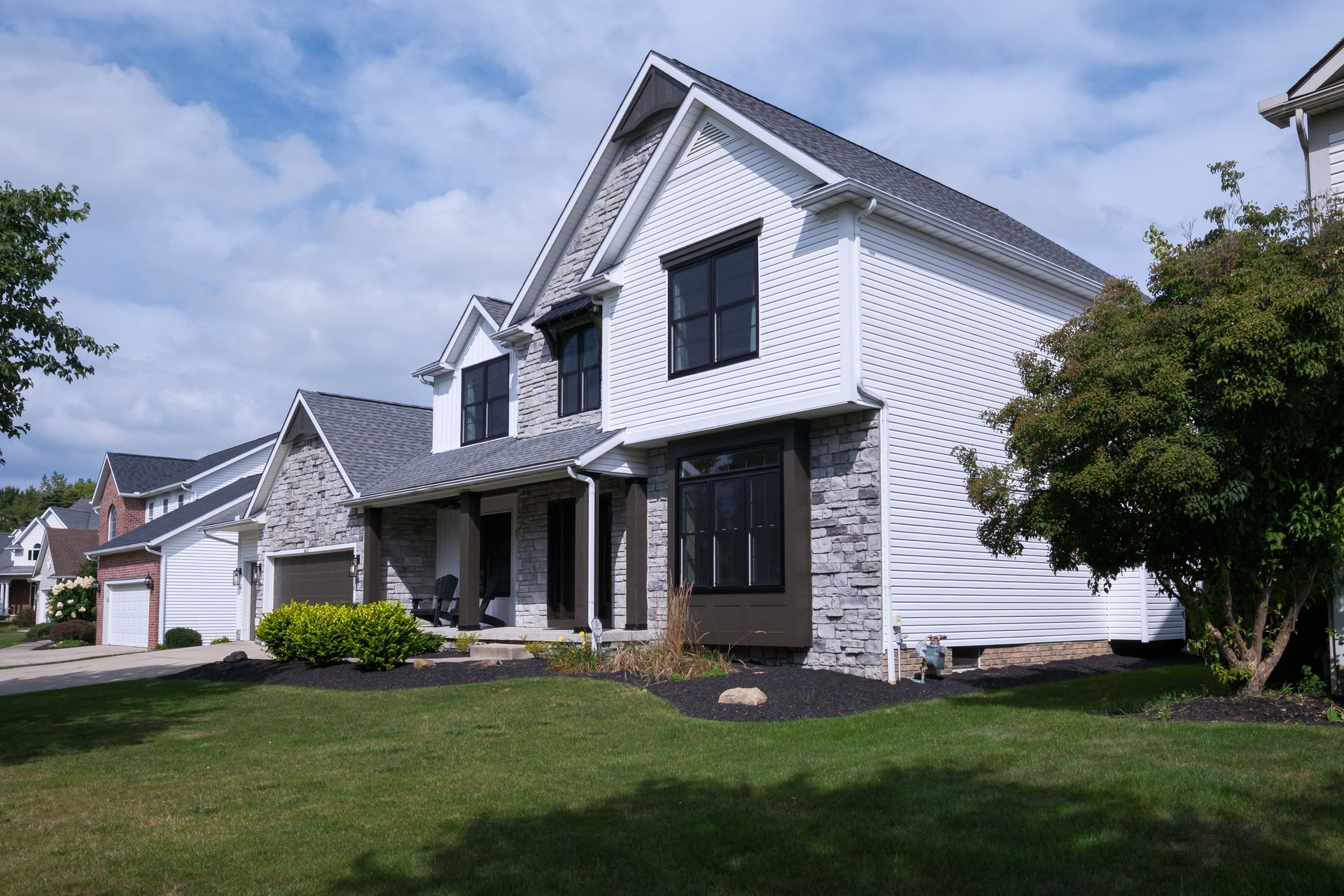 White and gray house with black windows under a blue sky, green lawn and tree in front.