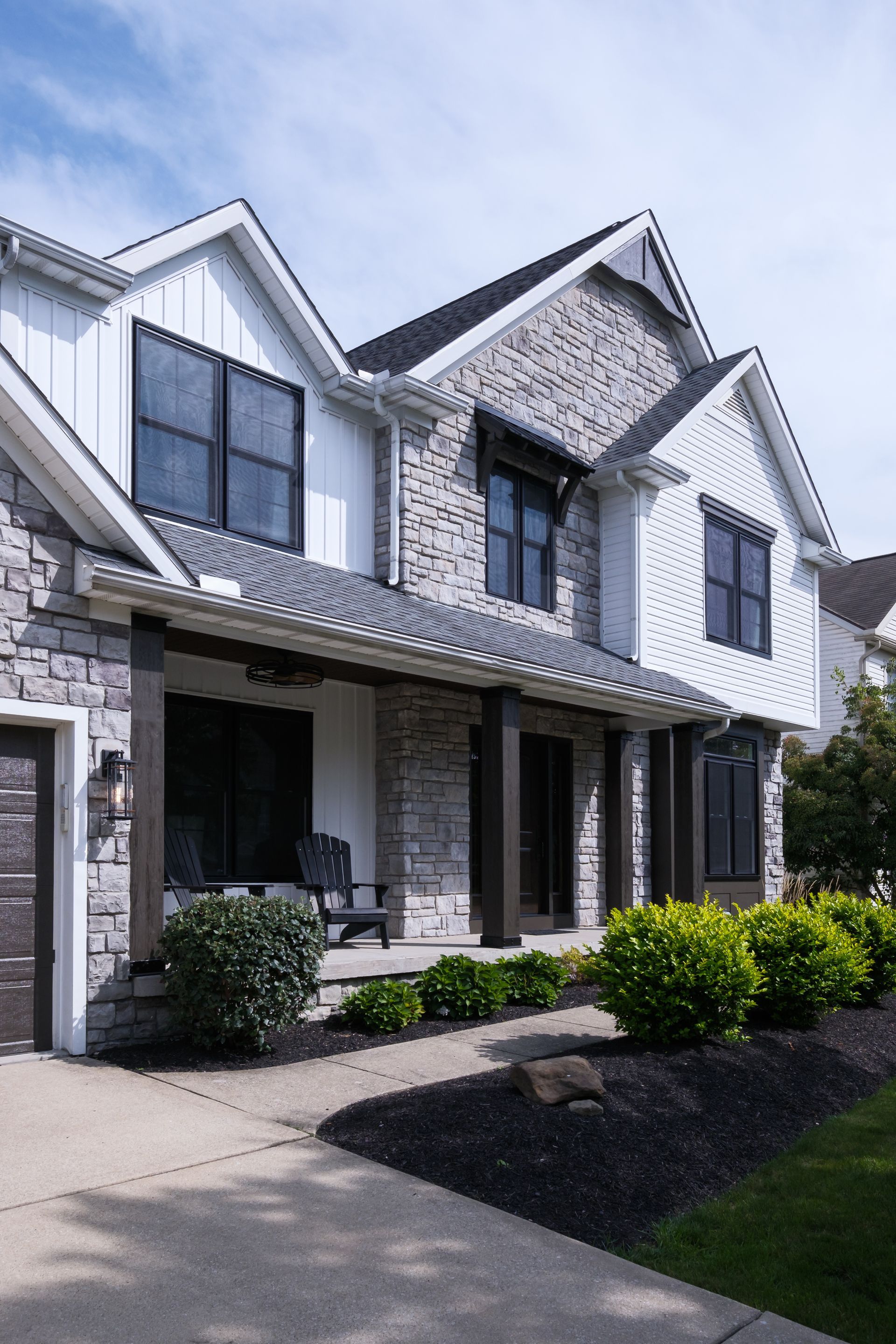 Two-story house with stone and white siding, black windows, a porch, and a paved walkway.