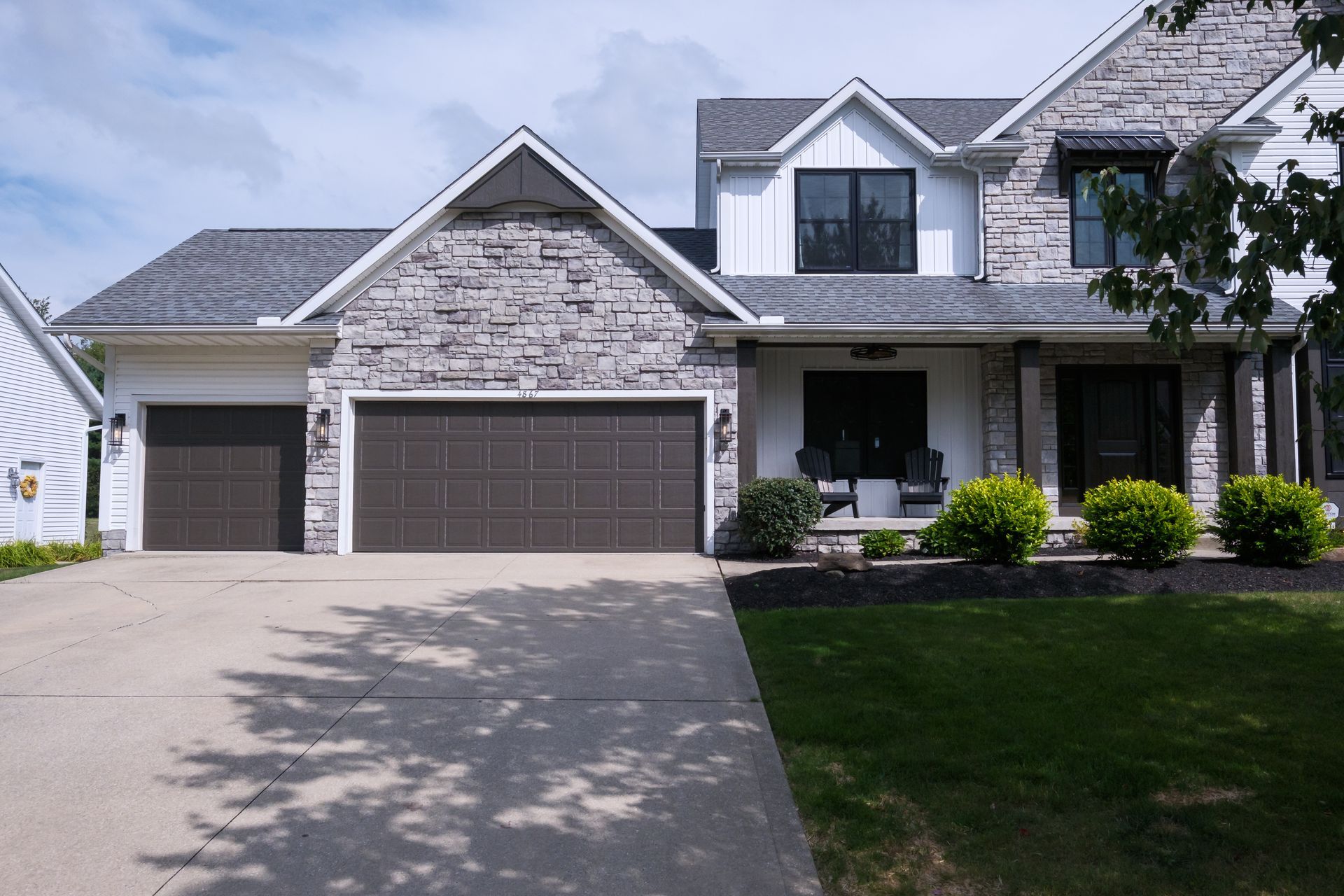Two-story house with gray stone accents, brown garage doors, and a front porch.