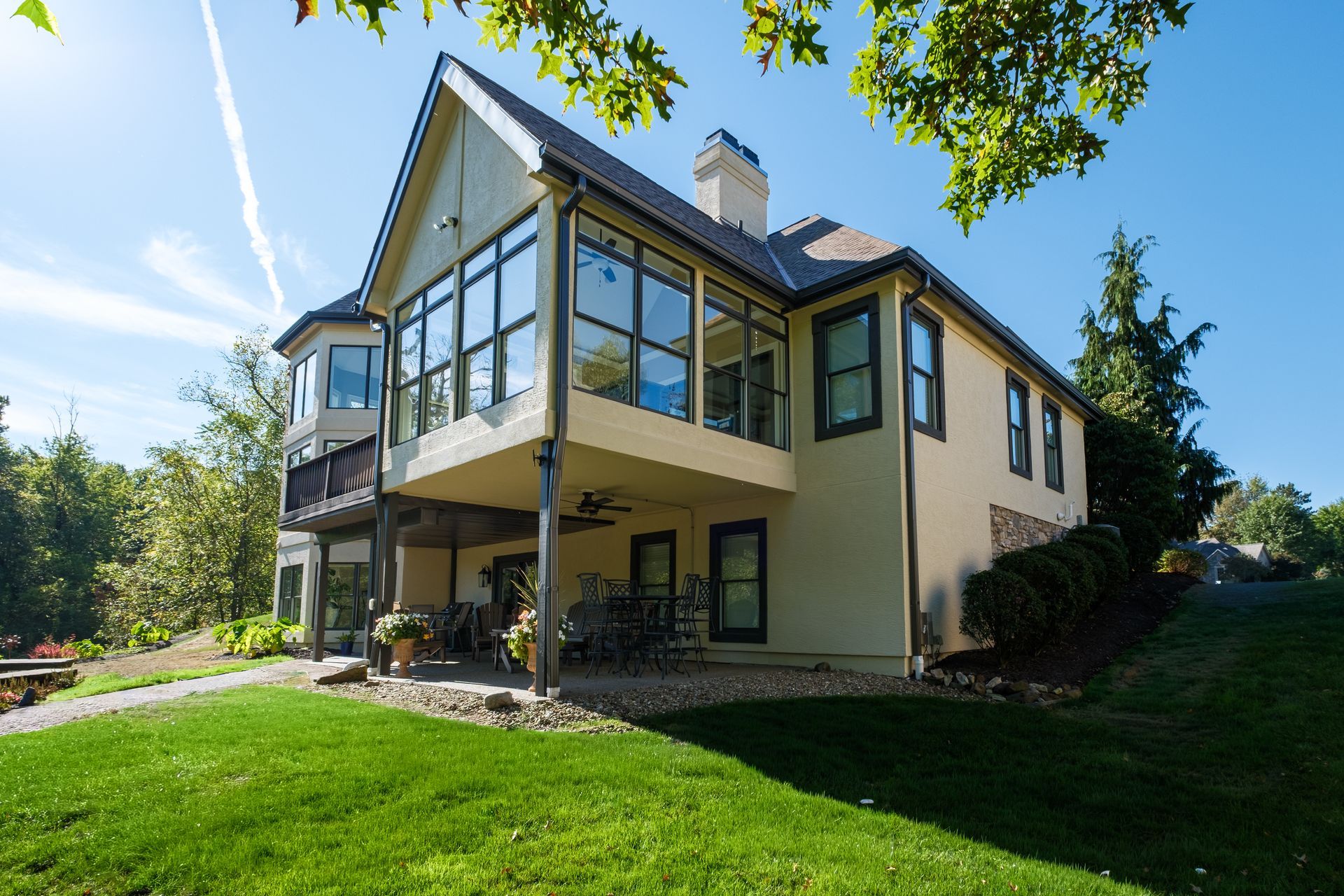 Beige house with large windows, balcony, and green lawn under a bright blue sky.