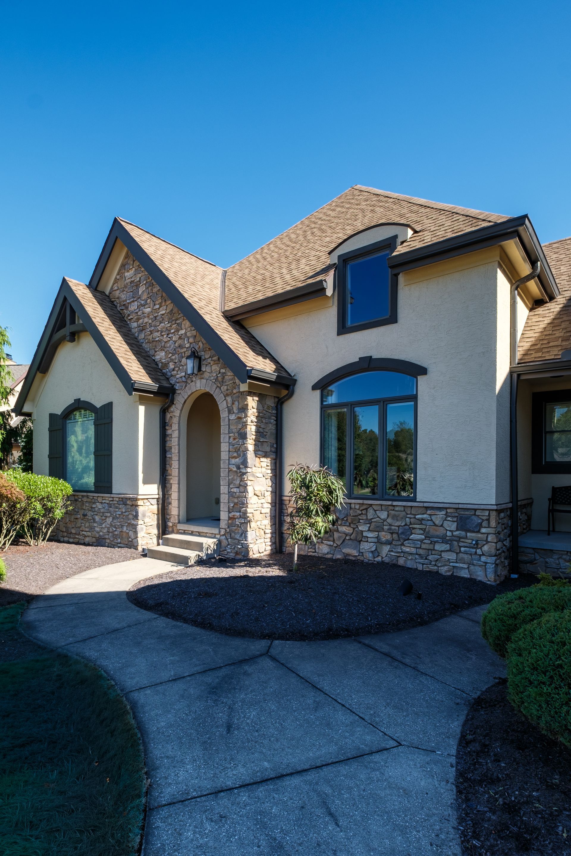 Tan stucco home with stone accents, arched entryway, and blue sky.