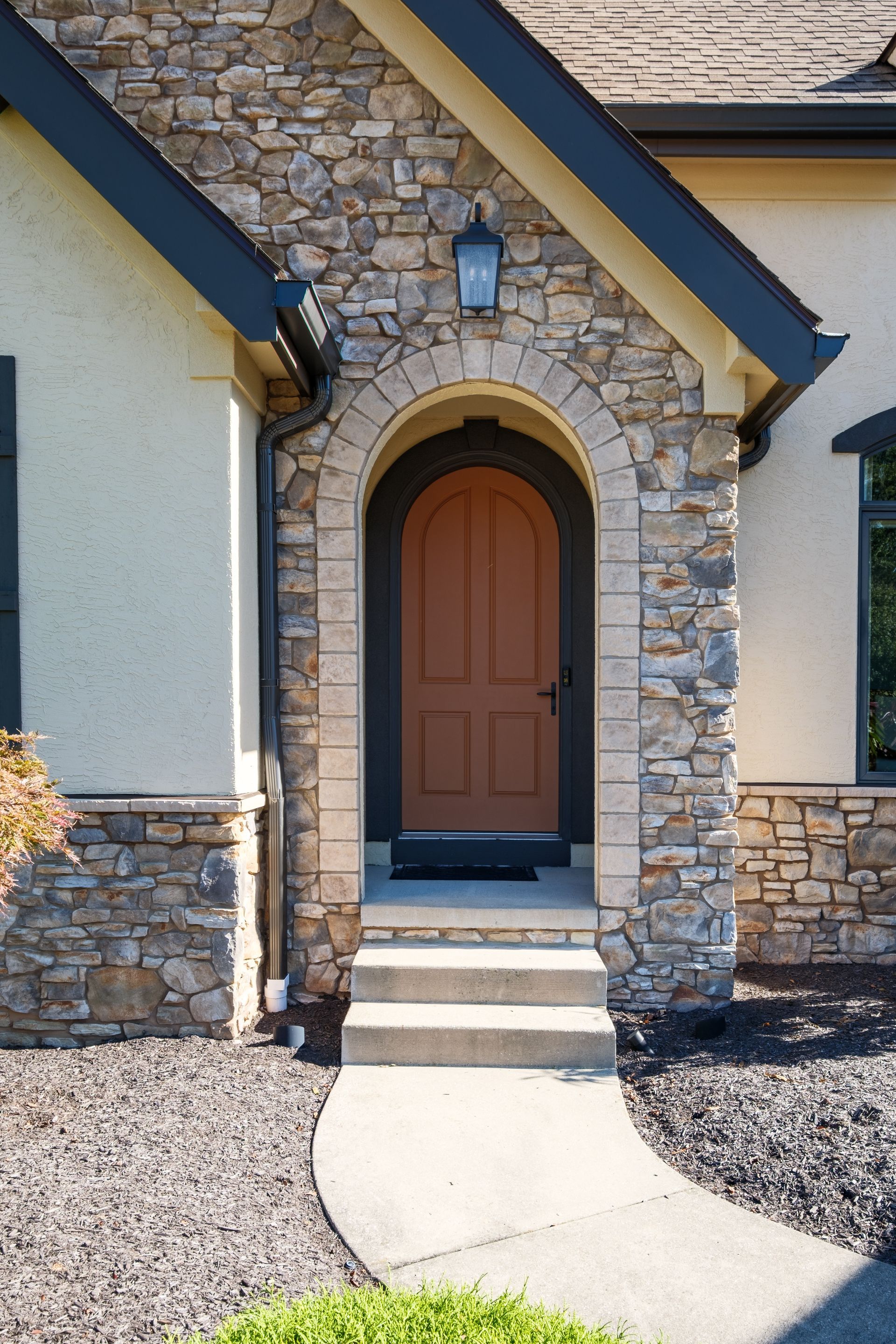 Stone-framed arched doorway with brown door, steps, and walkway leading to it.