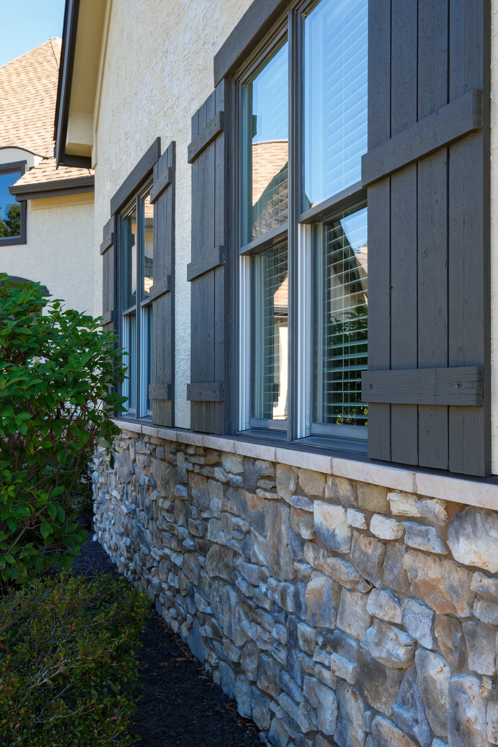 House exterior with stone foundation, gray shutters, and windows.