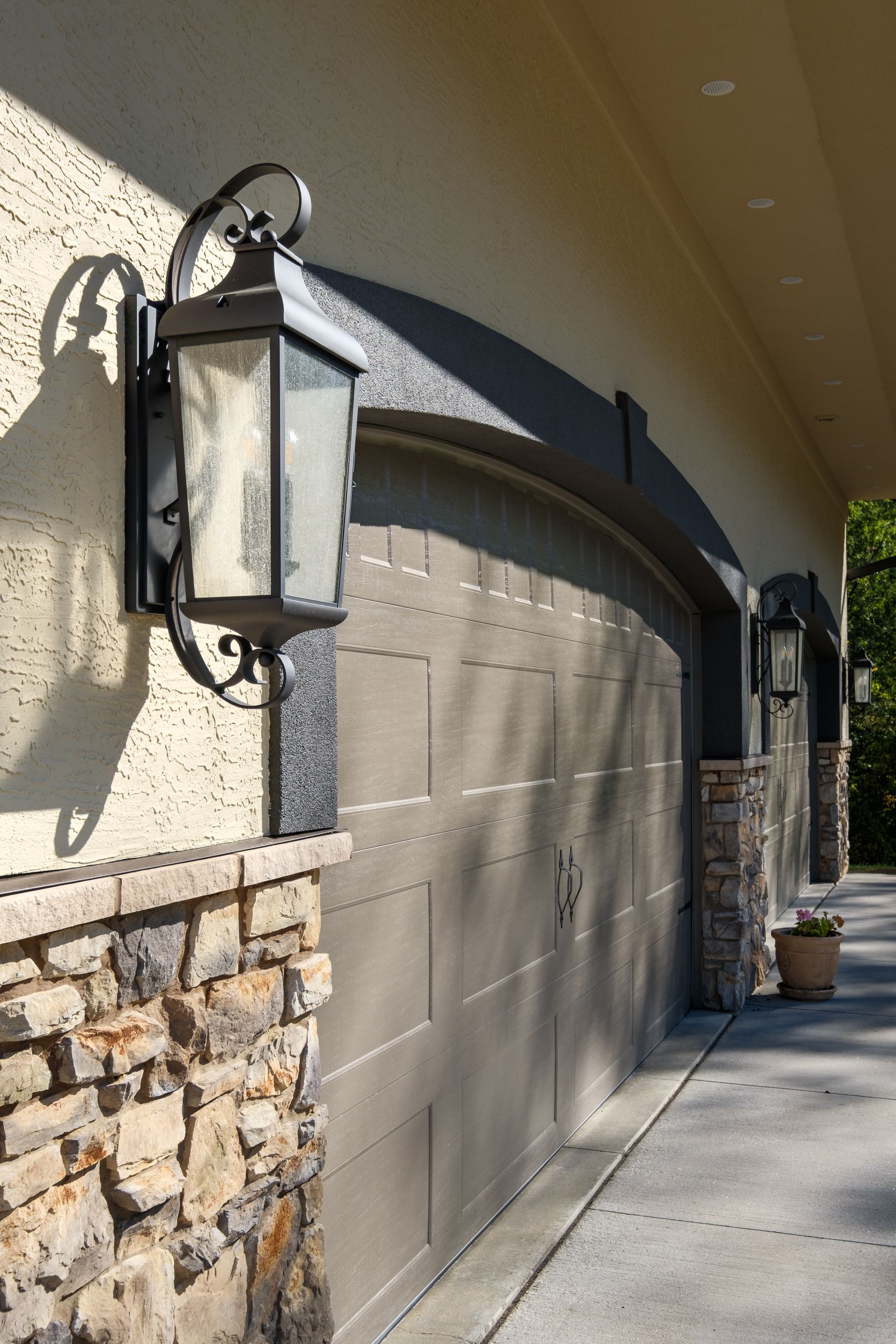 Exterior of a garage with a tan door, stone accents, and black lantern-style lights.