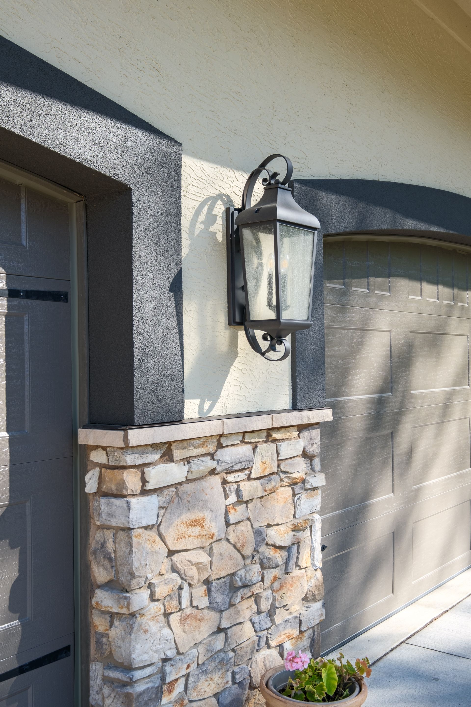 Black lantern on beige wall with stone accent below.
