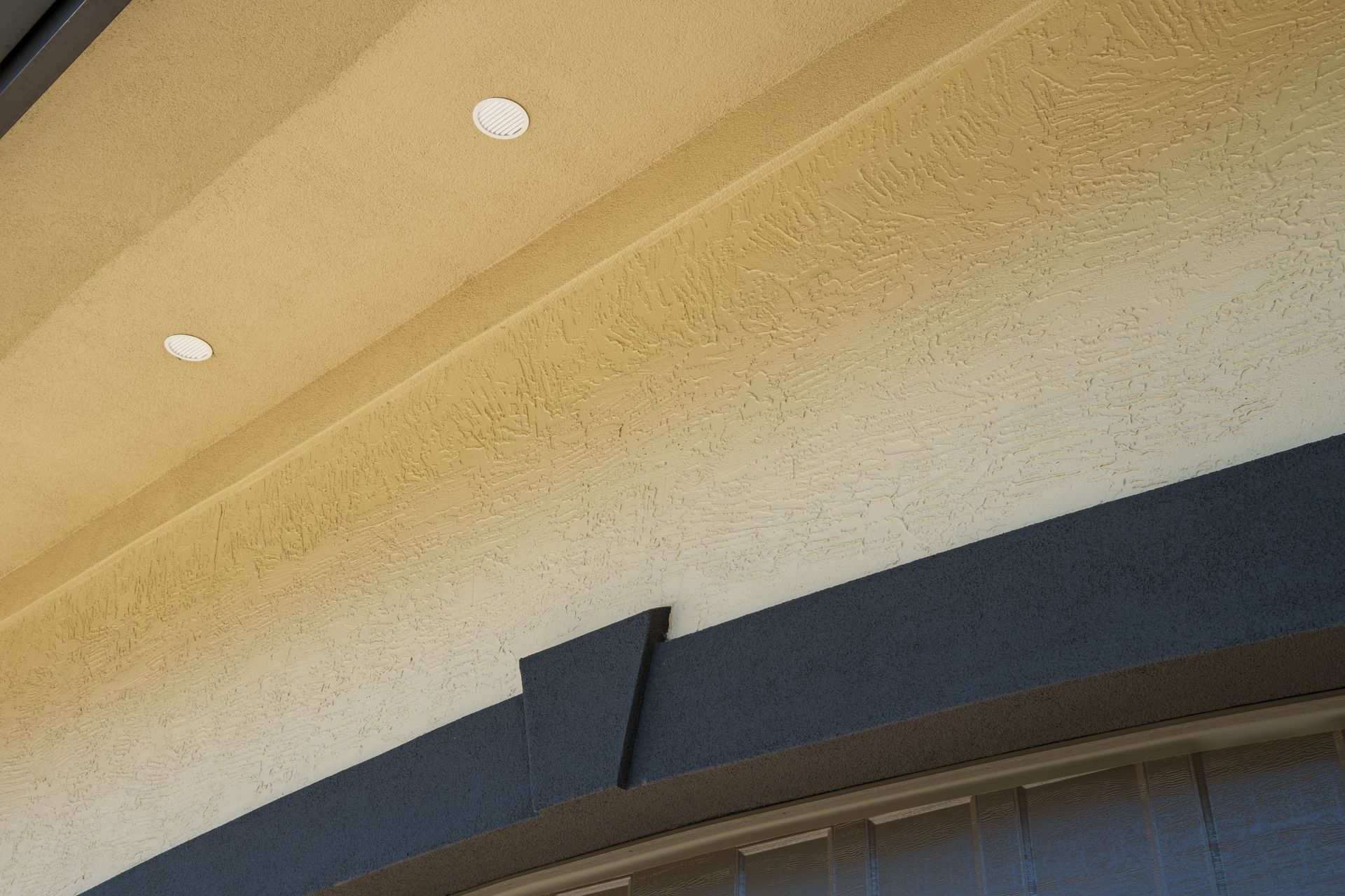 Beige textured exterior with dark gray trim and recessed white lights.