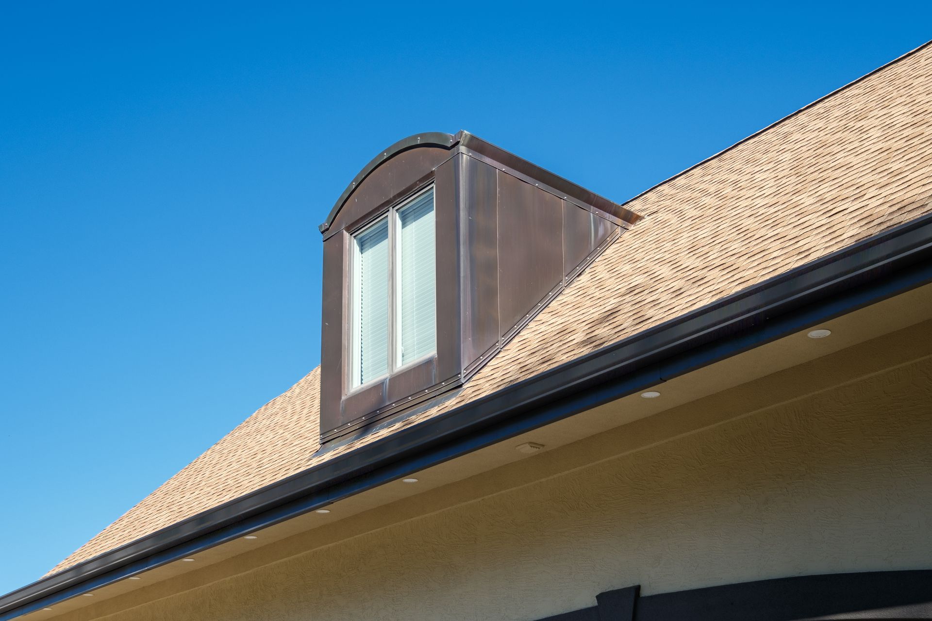 Brown copper-clad dormer on a beige shingle roof against a blue sky.