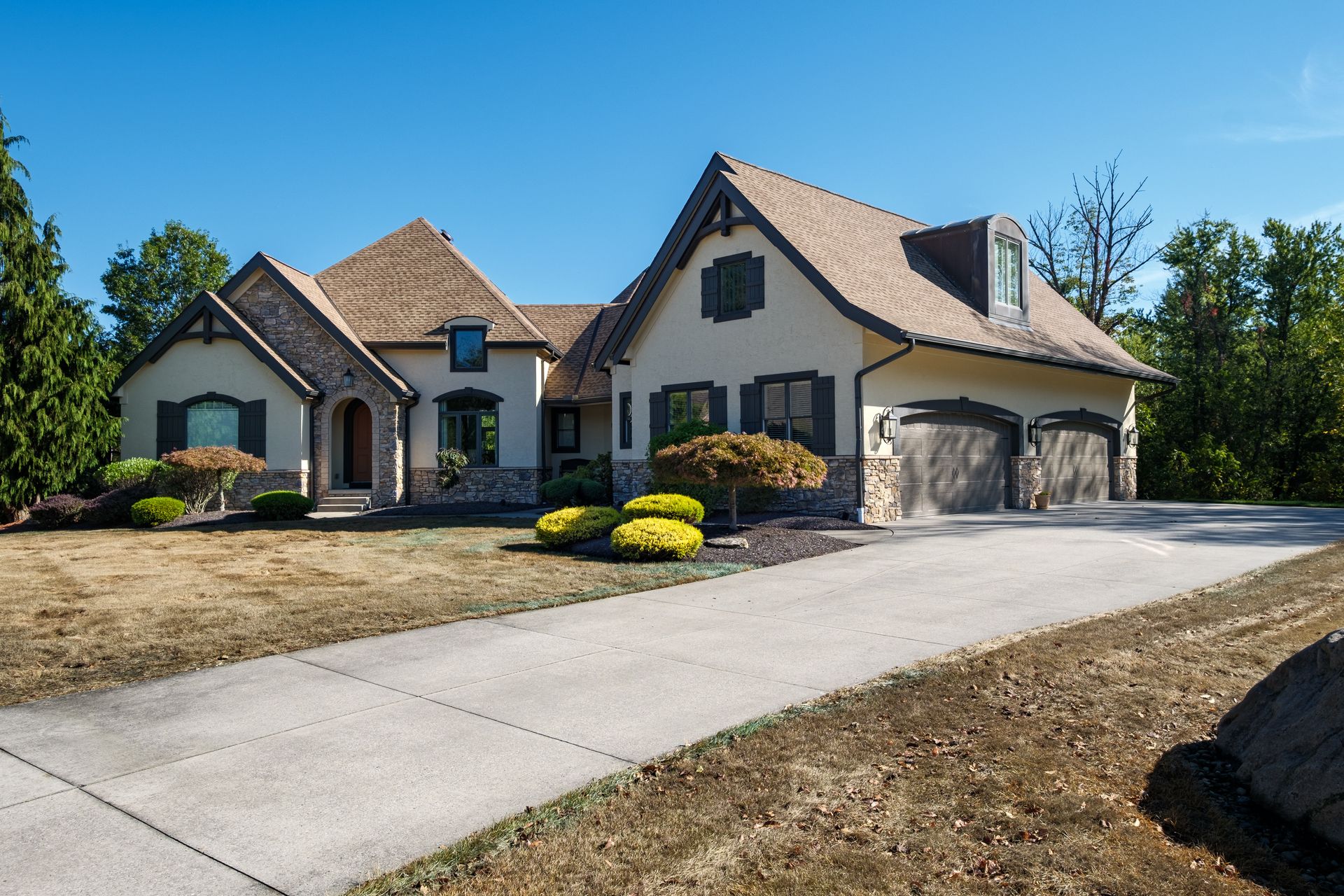 Beige house with a brown roof and a long driveway on a sunny day.