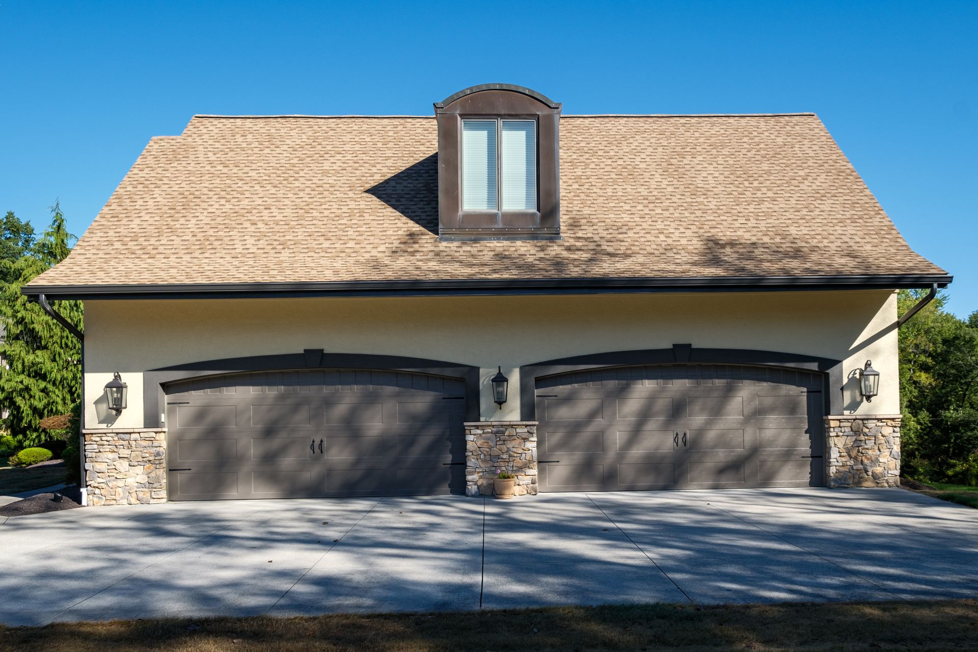 Two-car garage with tan exterior, stone accents, and brown garage doors. A window sits atop the roof.