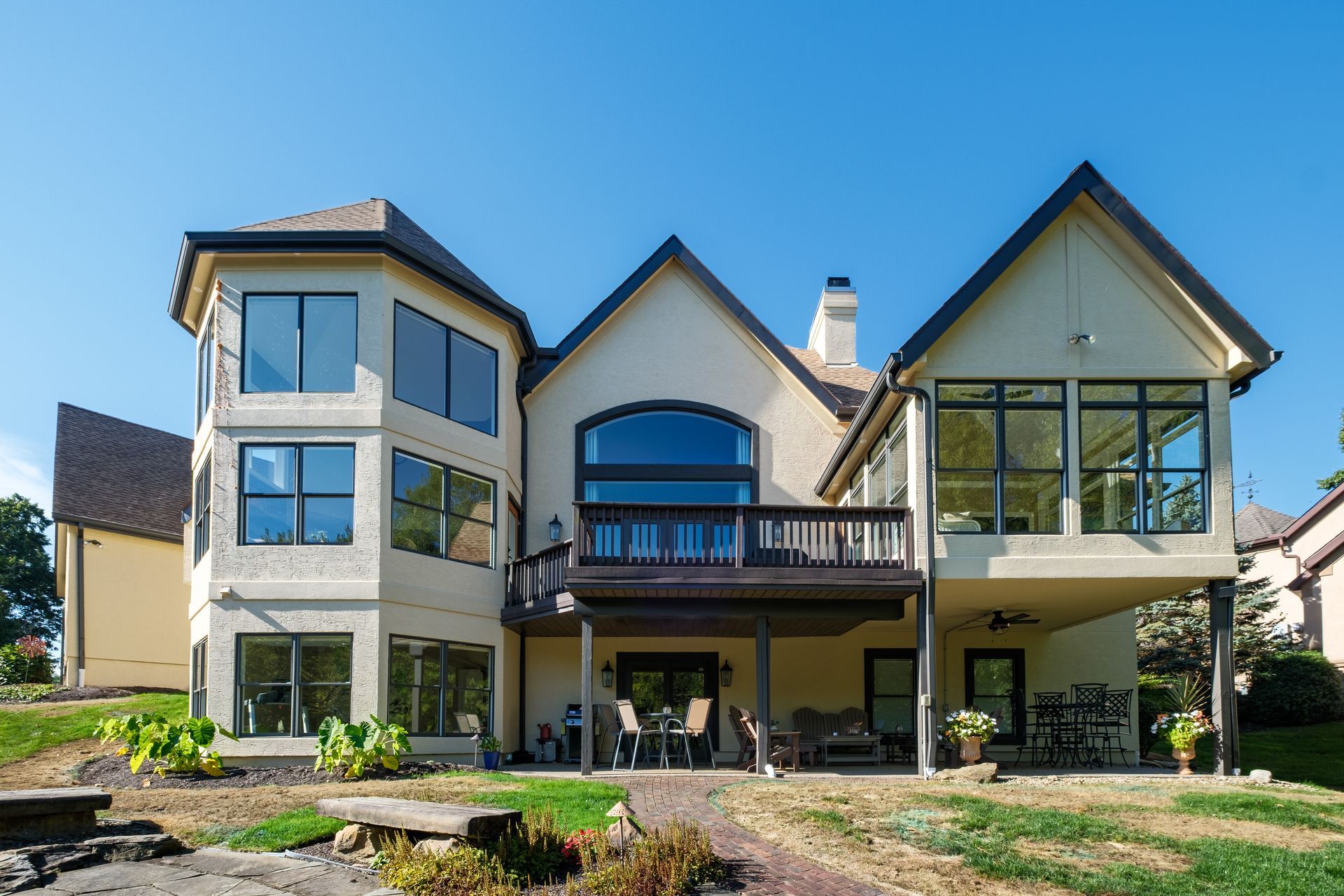 Rear view of a beige house with multiple windows and a deck, under a bright blue sky.