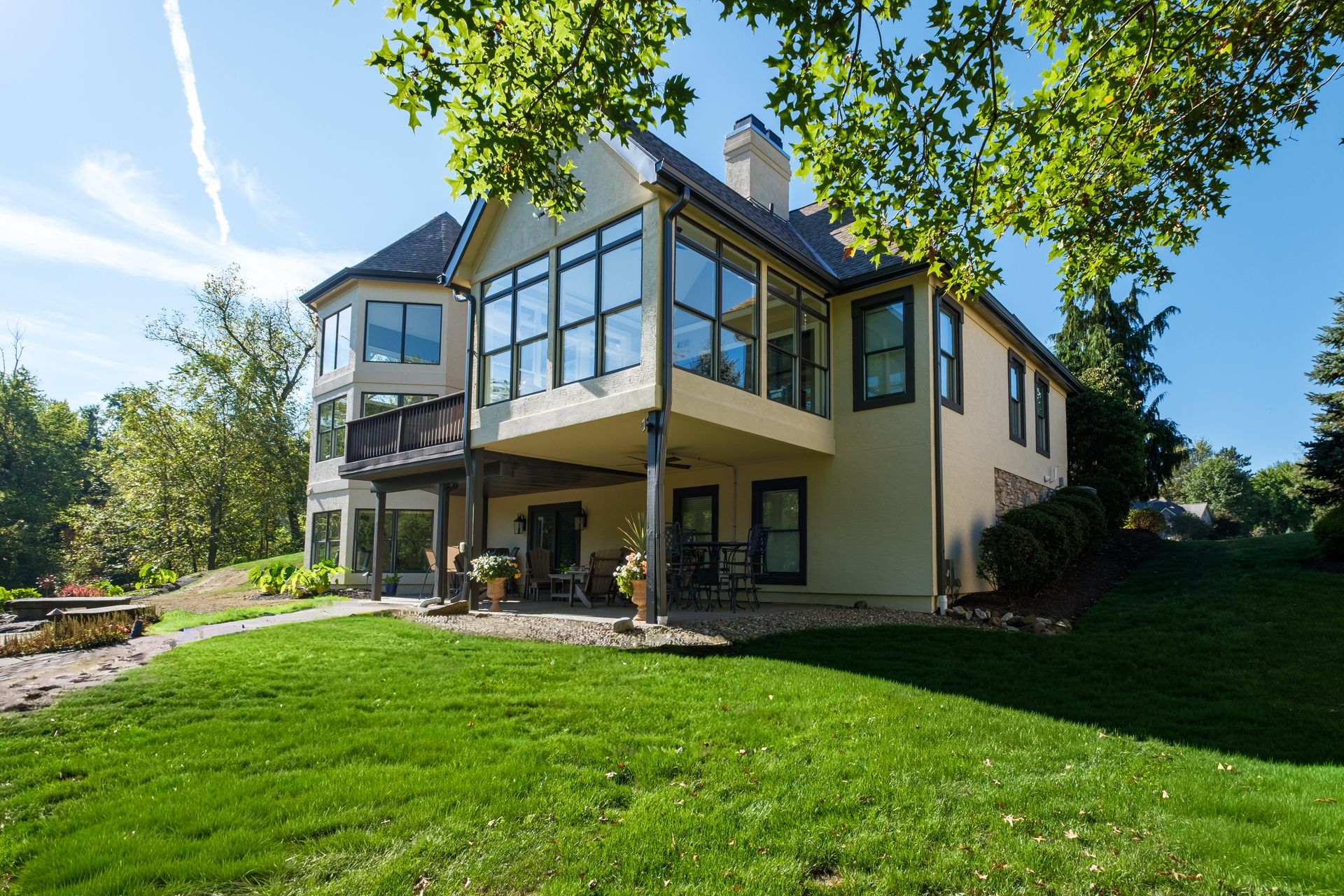 Two-story house with large windows, balcony, and green lawn on a sunny day.