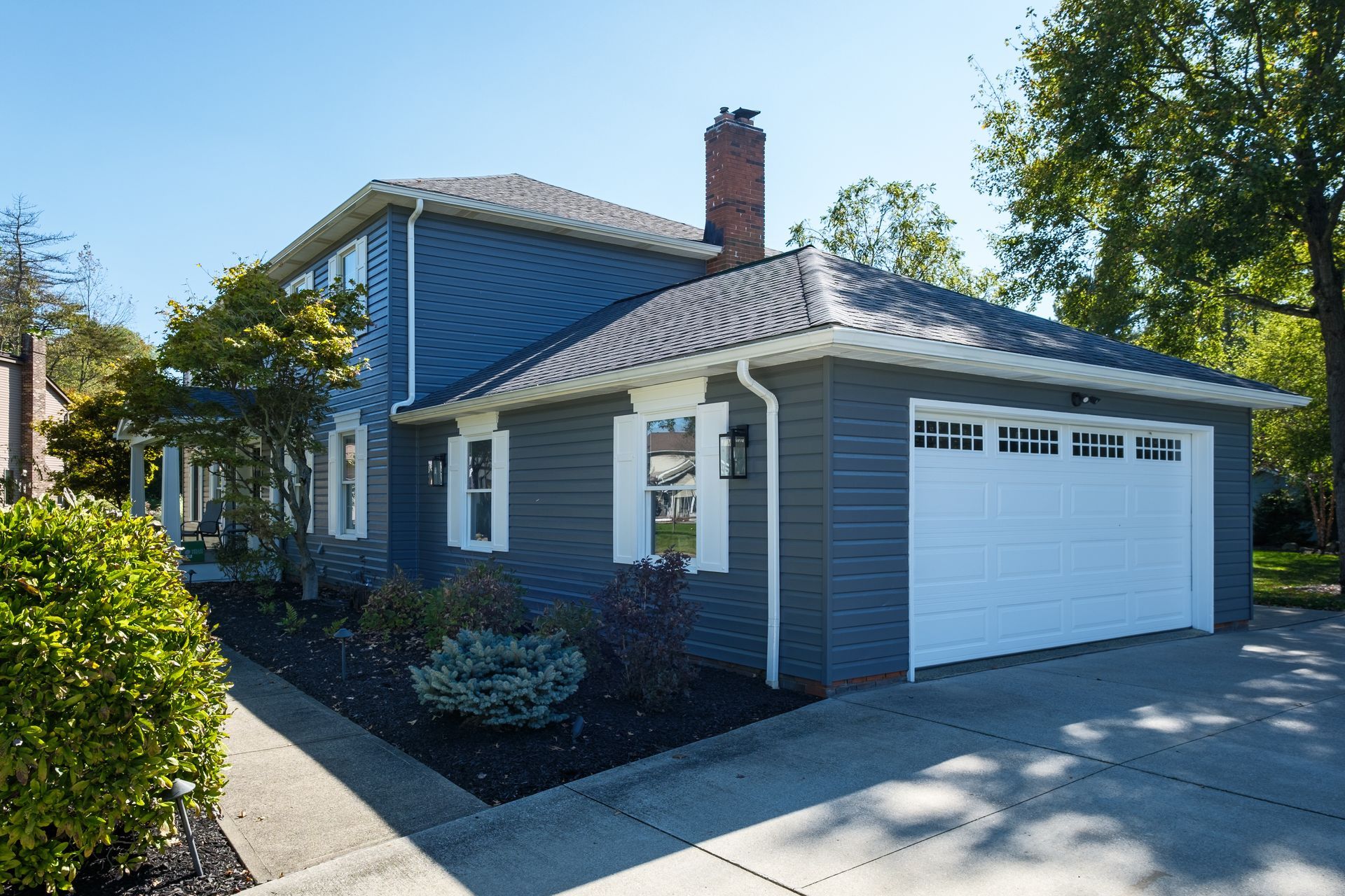 Blue house with white trim, garage, and chimney, under a bright blue sky.
