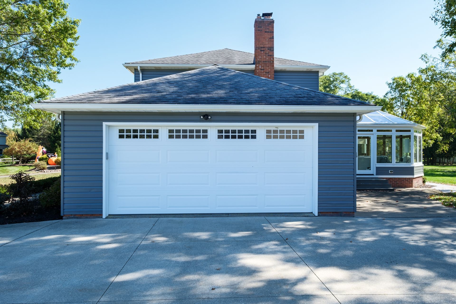 Gray garage with white door, attached to a house with a sunroom.