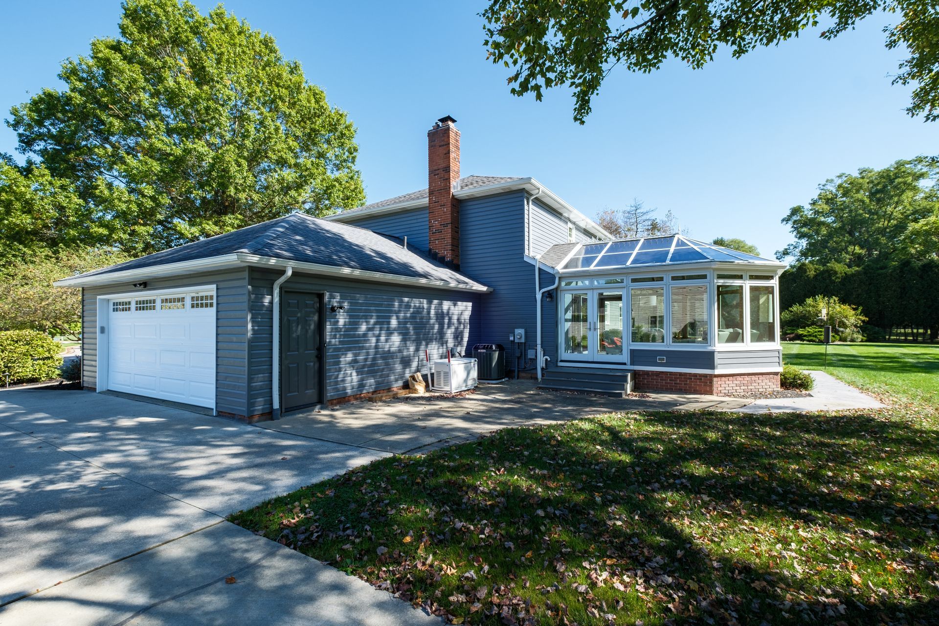 Blue house with attached garage and glass-walled sunroom on a sunny day.