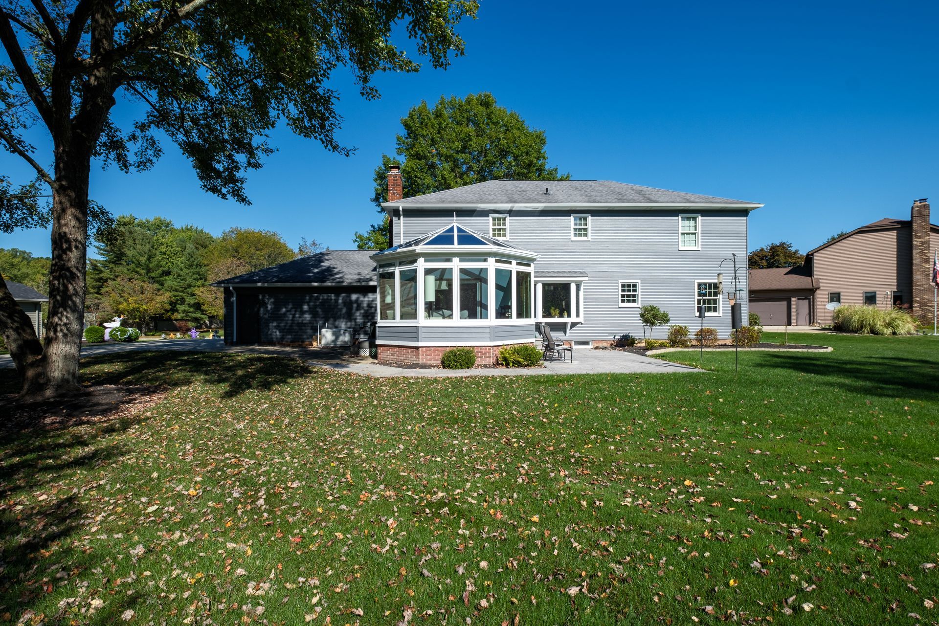 Backyard of a two-story gray house with sunroom and garage on a sunny day.