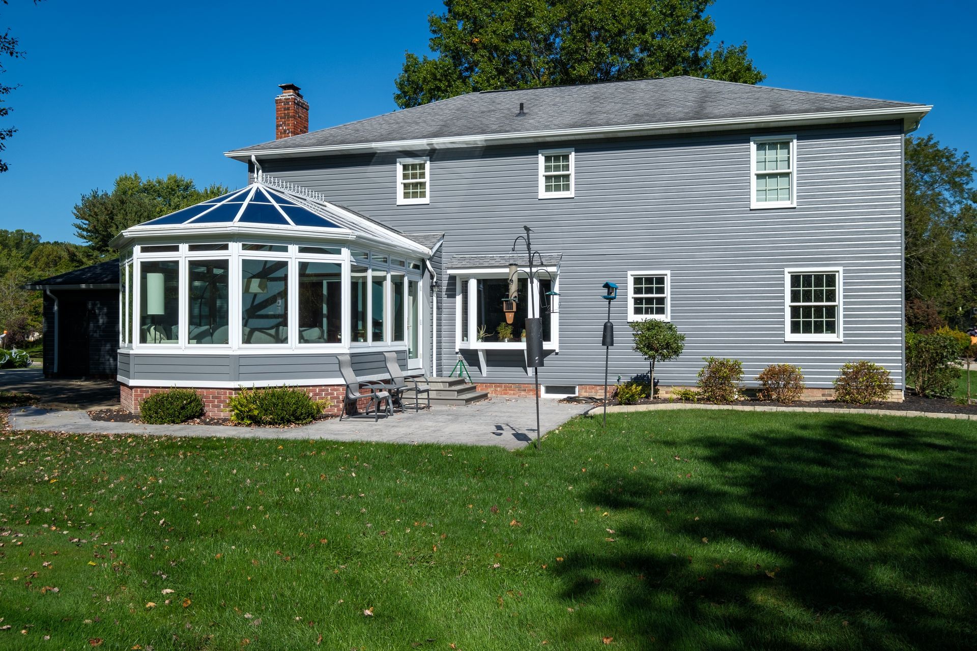 Gray house with a sunroom, patio, and green lawn under a blue sky.