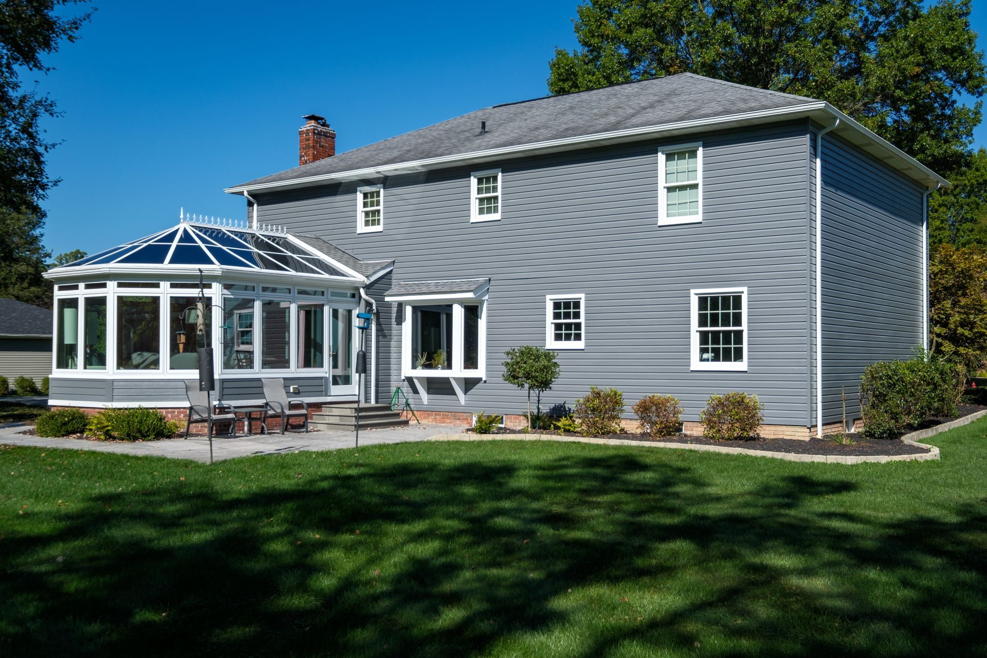 Gray house with a sunroom, green lawn, and blue sky.