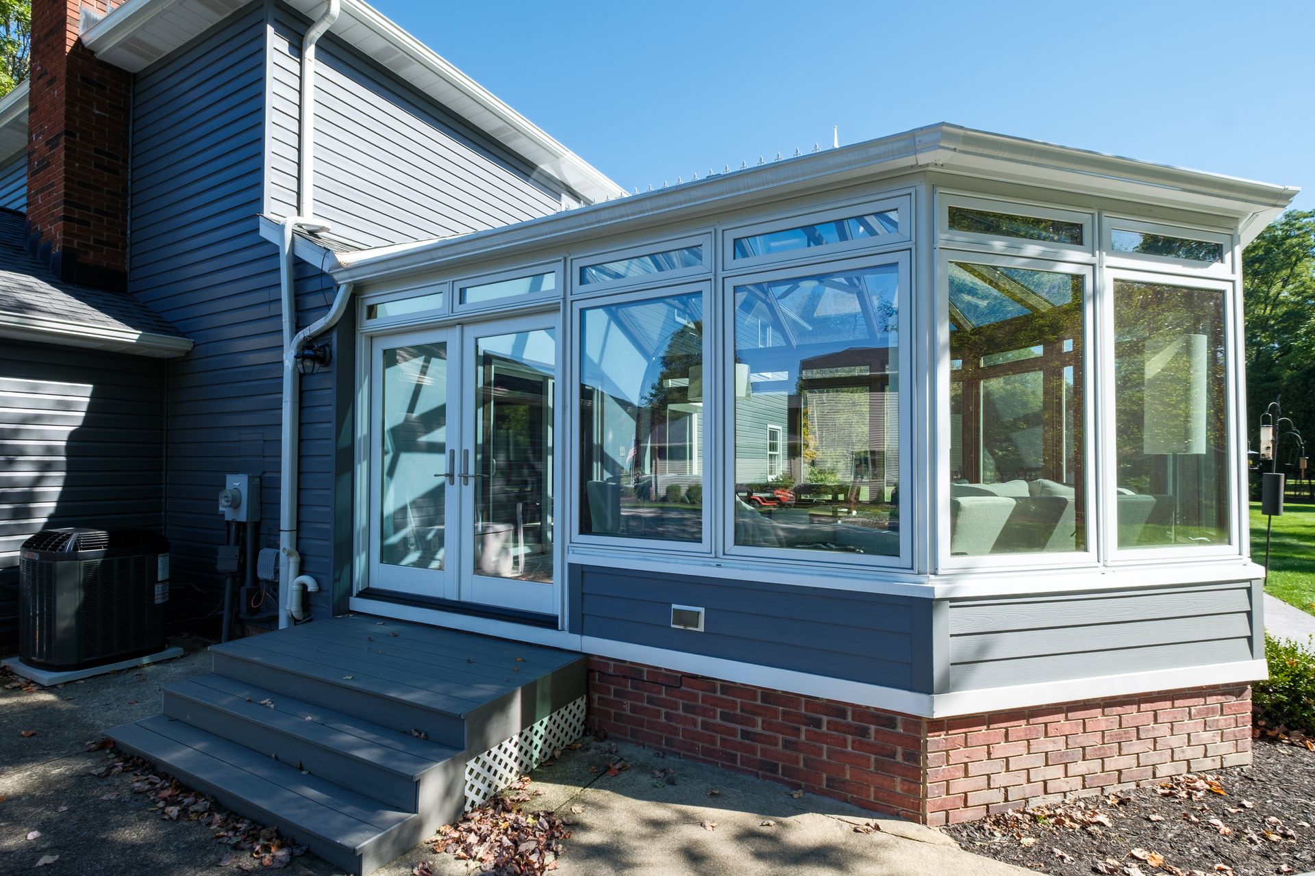 Sunroom addition on a house with large windows, blue siding, brick foundation, and steps.