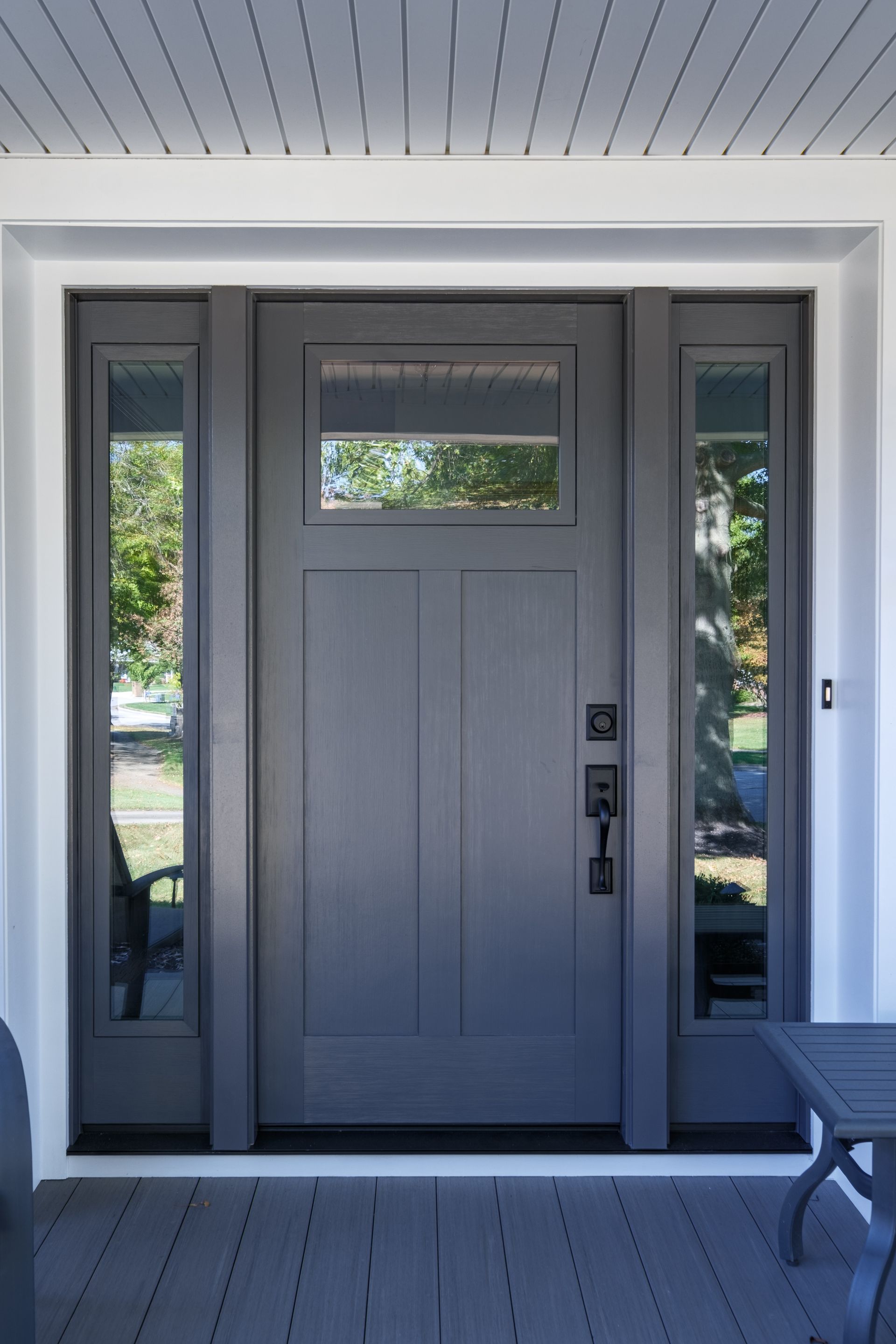 Gray front door with sidelights, black hardware, on a porch.