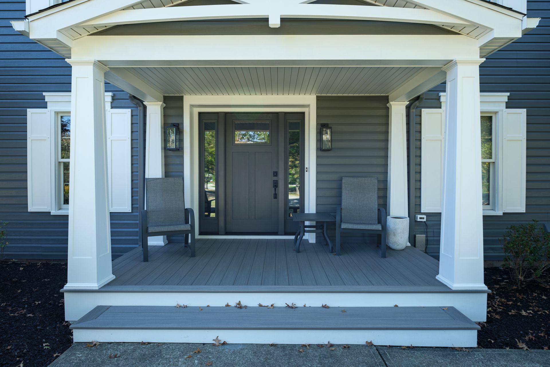 Gray home porch with white columns, gray chairs, and dark front door.